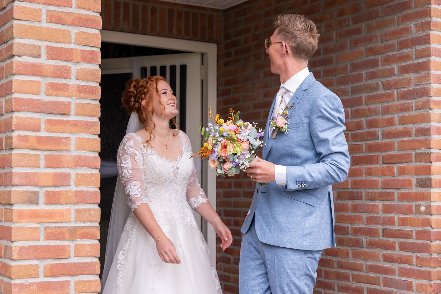 A romantic first look moment between newlyweds at a brick house entrance.