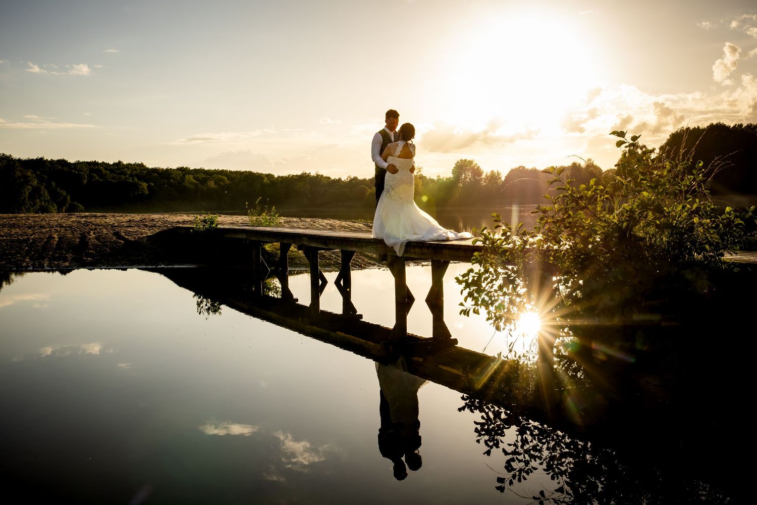 Silhouettes of a wedding couple and guests walking along a lake at sunset.