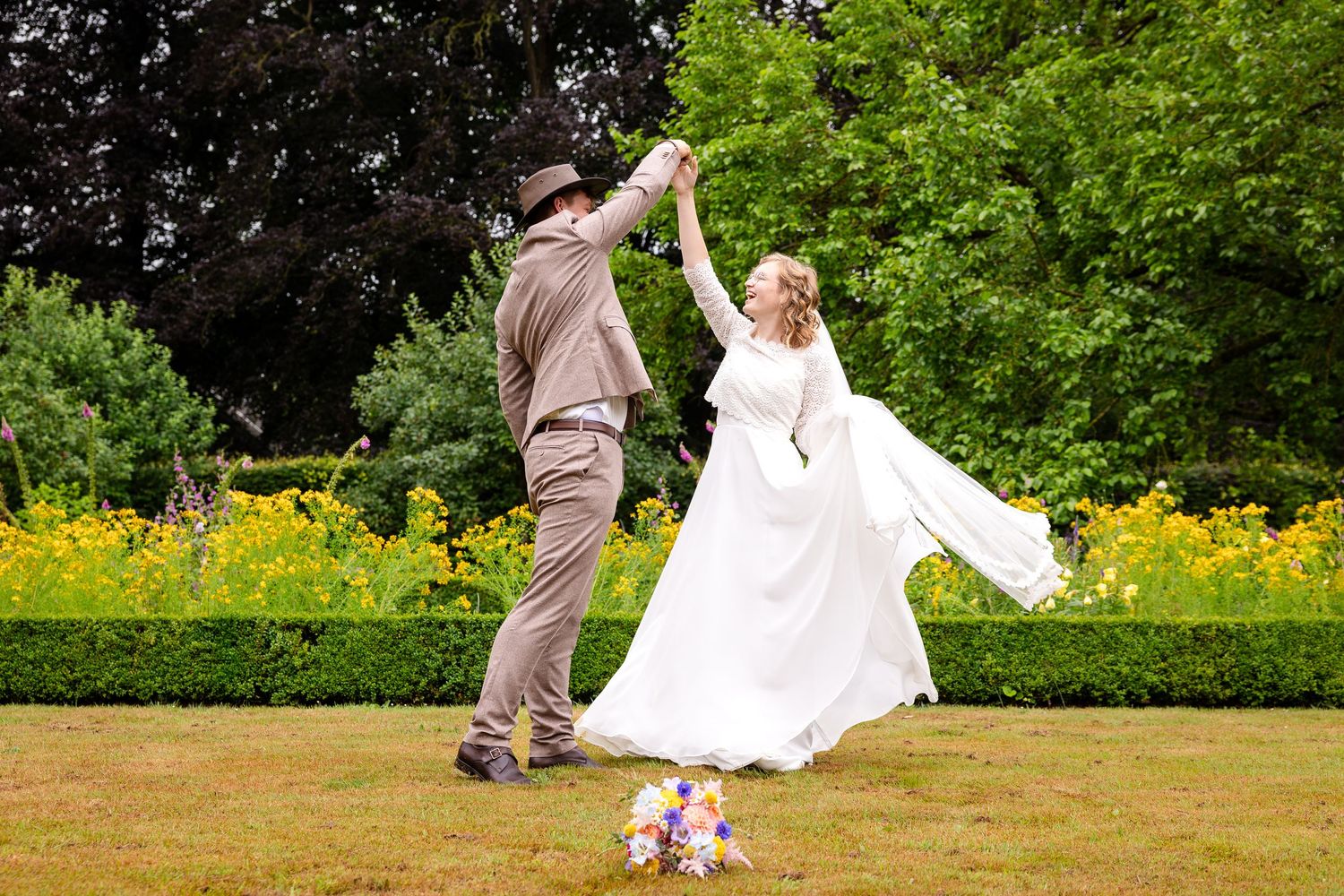 A couple dances joyfully in a garden setting with yellow wildflowers and lush greenery in the background.