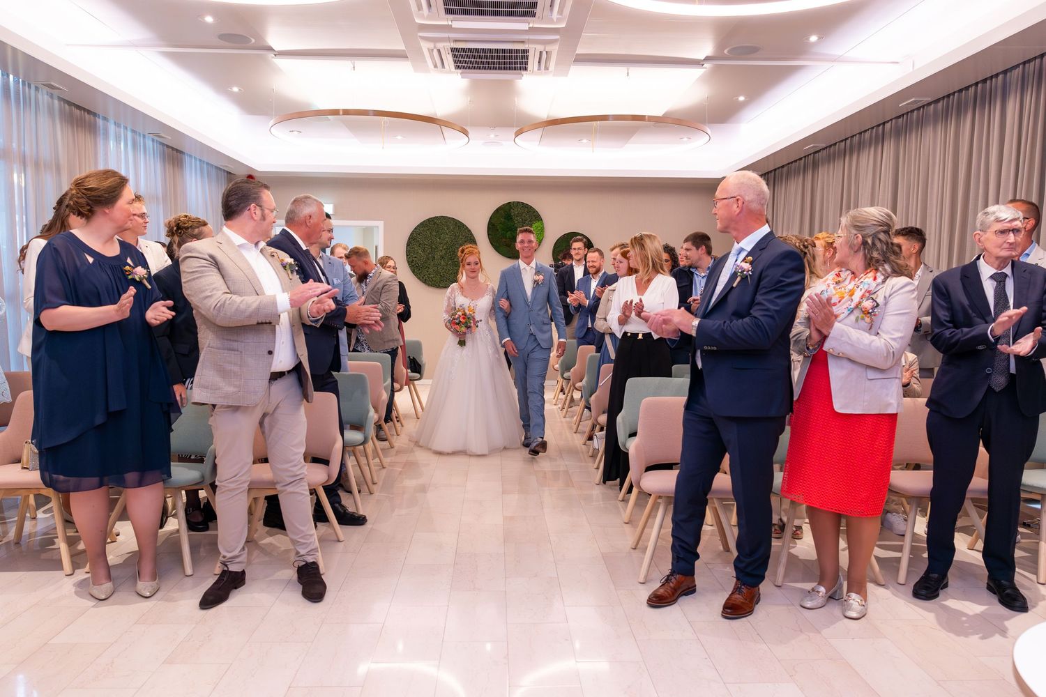 Wedding ceremony guests line modern indoor hallway while taking photos with phones.