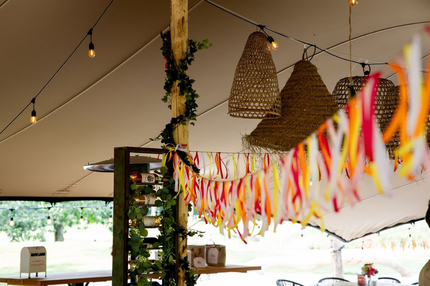 Rustieke bruiloftsdecoratie met geweven hanglampen en kleurrijke linten die aan het plafond hangen.
