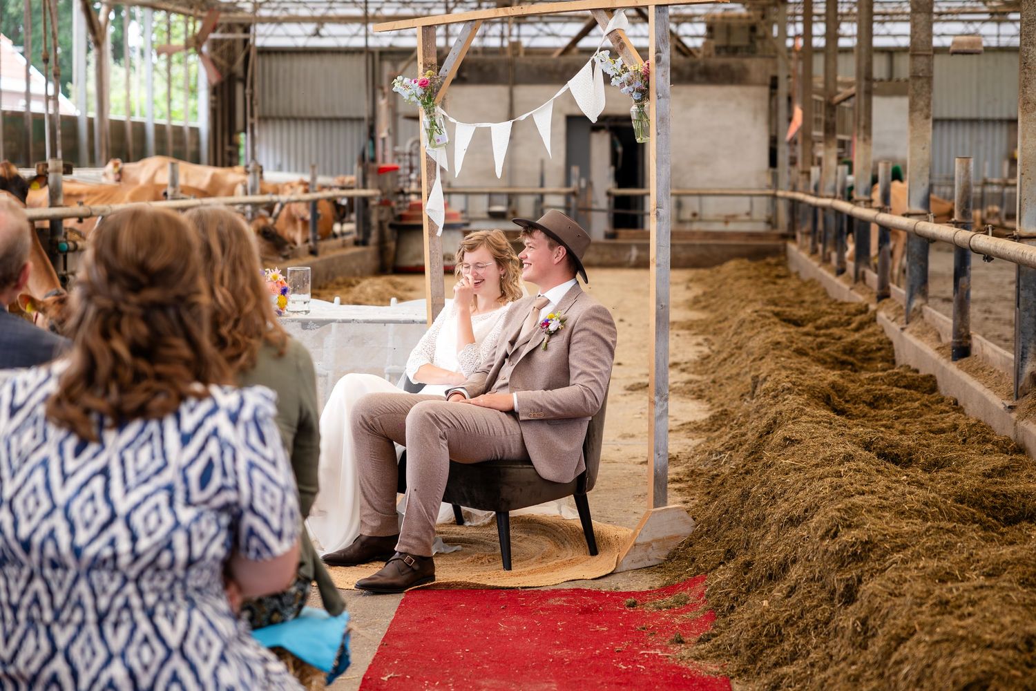 Wedding ceremony in progress inside a working barn with hay bales and white bunting decorations.