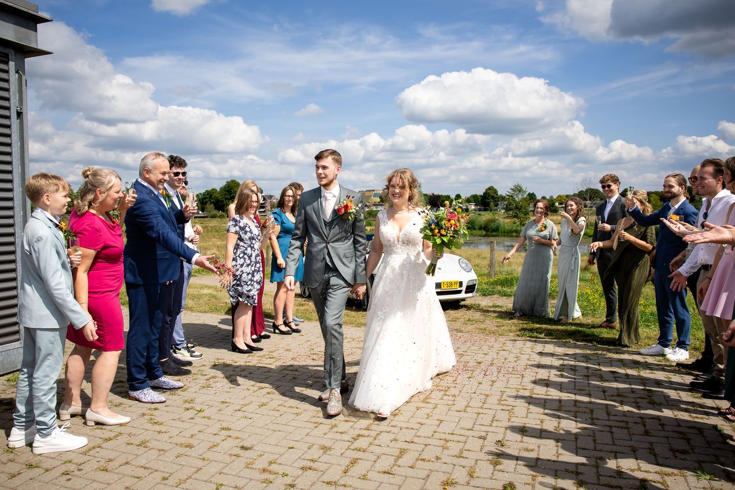 Wedding celebration with guests gathered on stone pathway under blue summer sky.