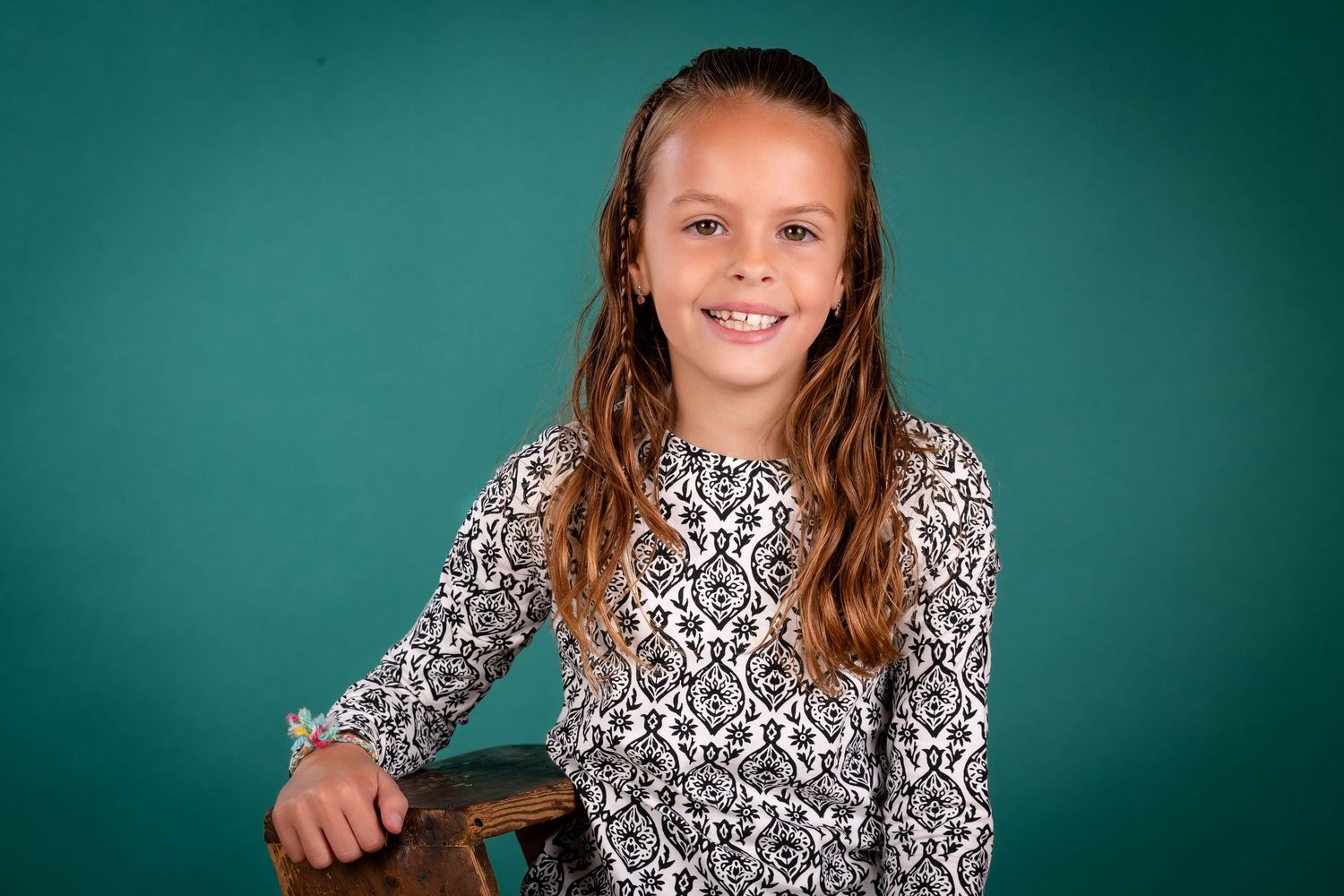 A student in a black and white patterned dress poses for a school portrait against a teal backdrop.
