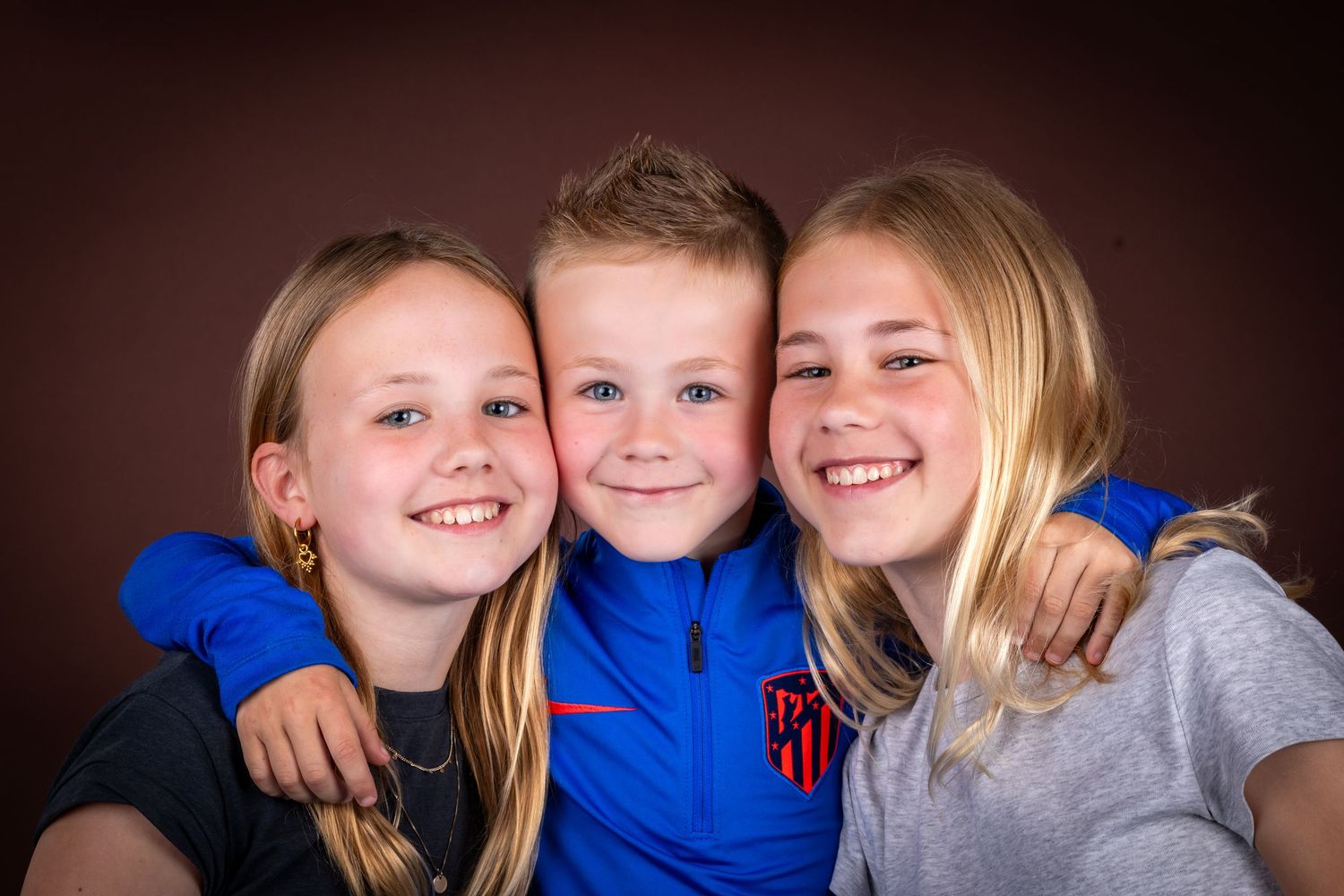 Three children hugging and smiling together in a warm studio portrait setting.