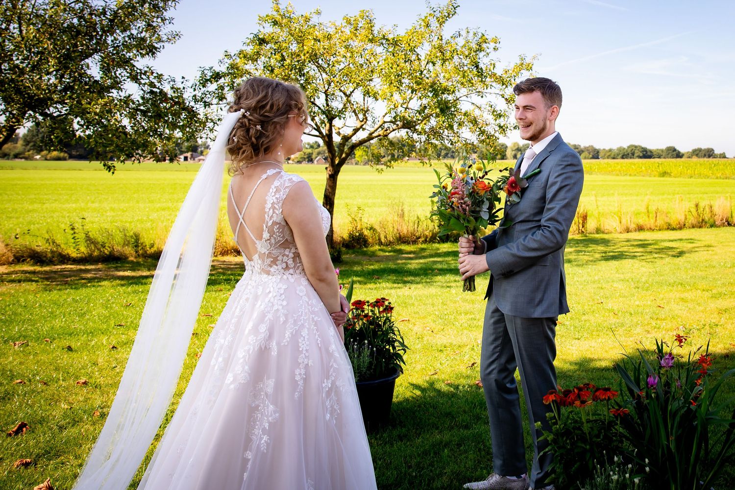 A romantic wedding photo in a sun-drenched field with a beautiful lace dress and grey suit.