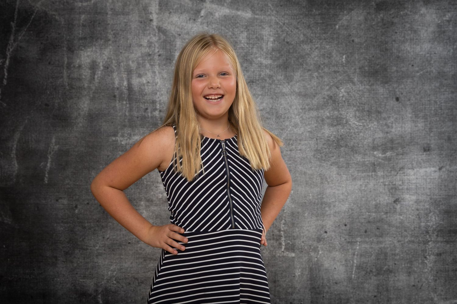 A person in a black and white striped dress poses in front of a gray textured background.