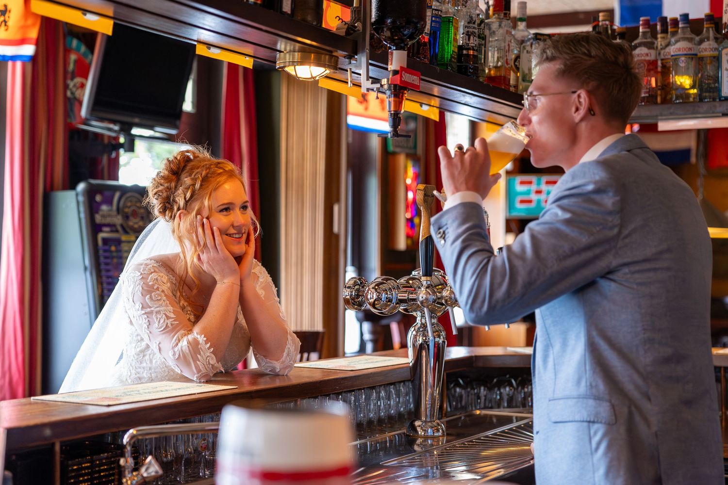 A couple shares a playful moment across a bar counter in a pub setting.