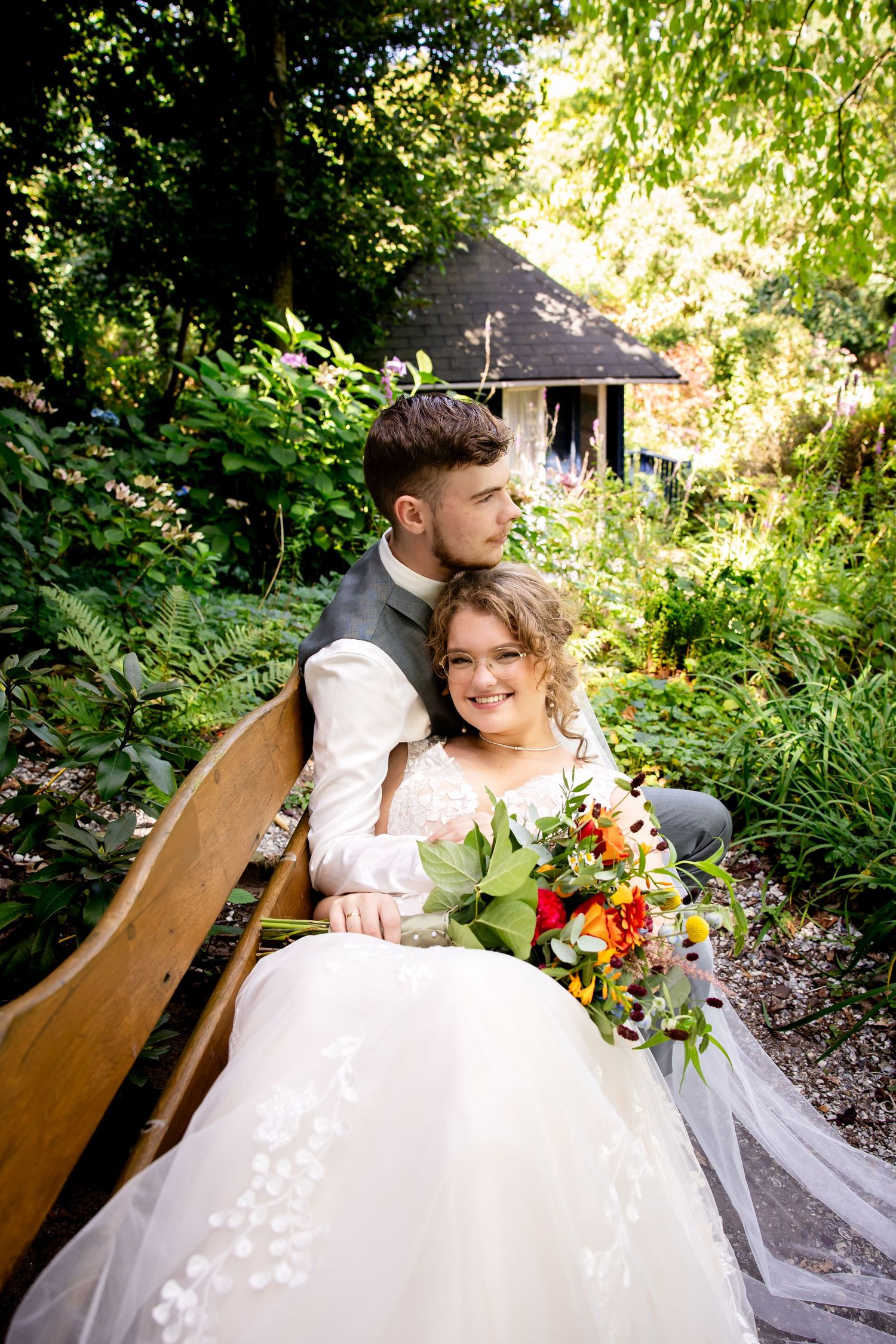 Romantic garden portrait with couple seated on wooden bench surrounded by greenery.