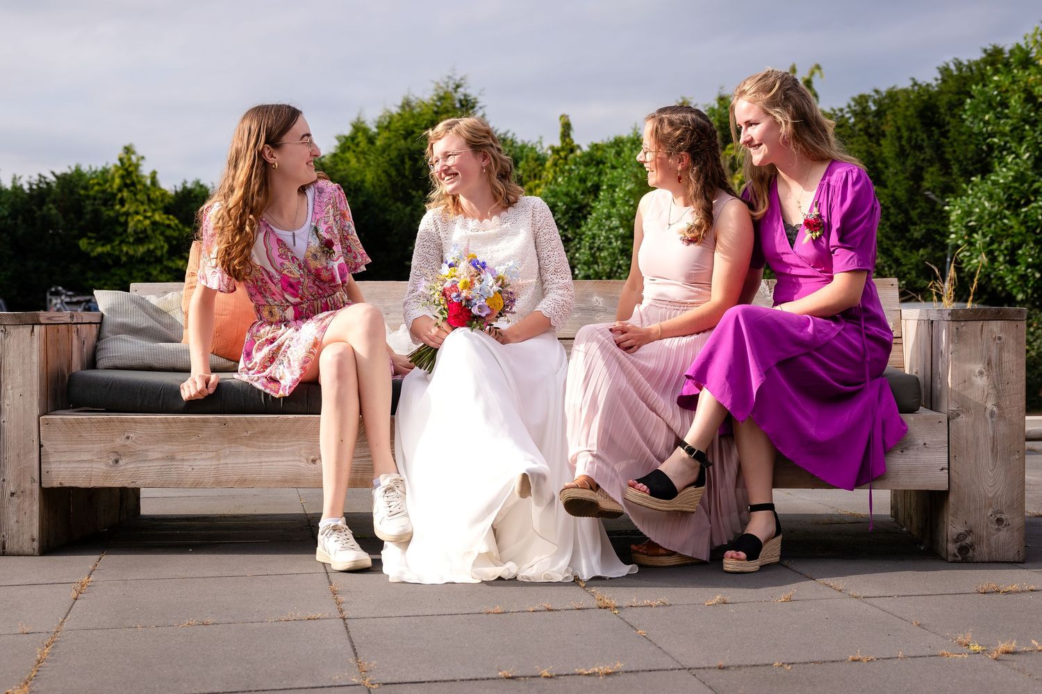 Wedding party relaxing on stone benches in a garden setting.