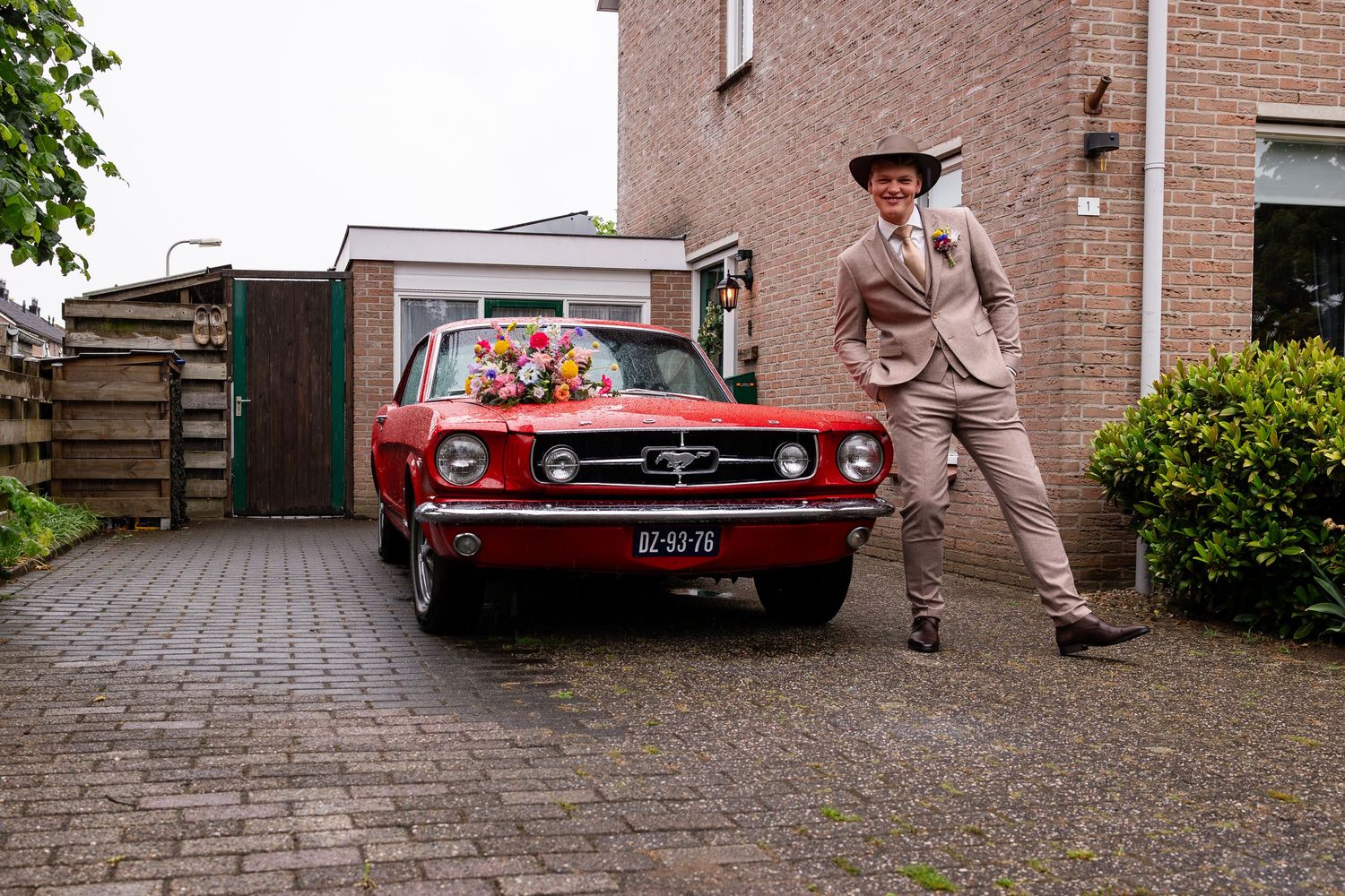 A classic red vintage car parked in front of a brick house.