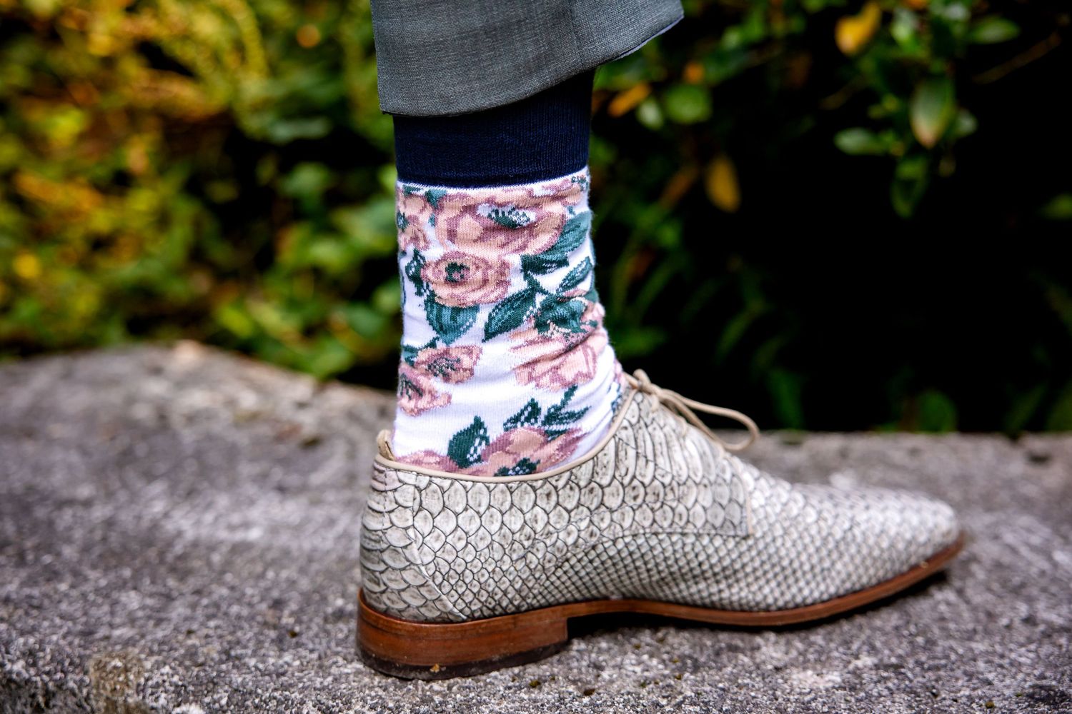 Close-up detail of floral patterned socks and beige oxford shoes on a stone surface.