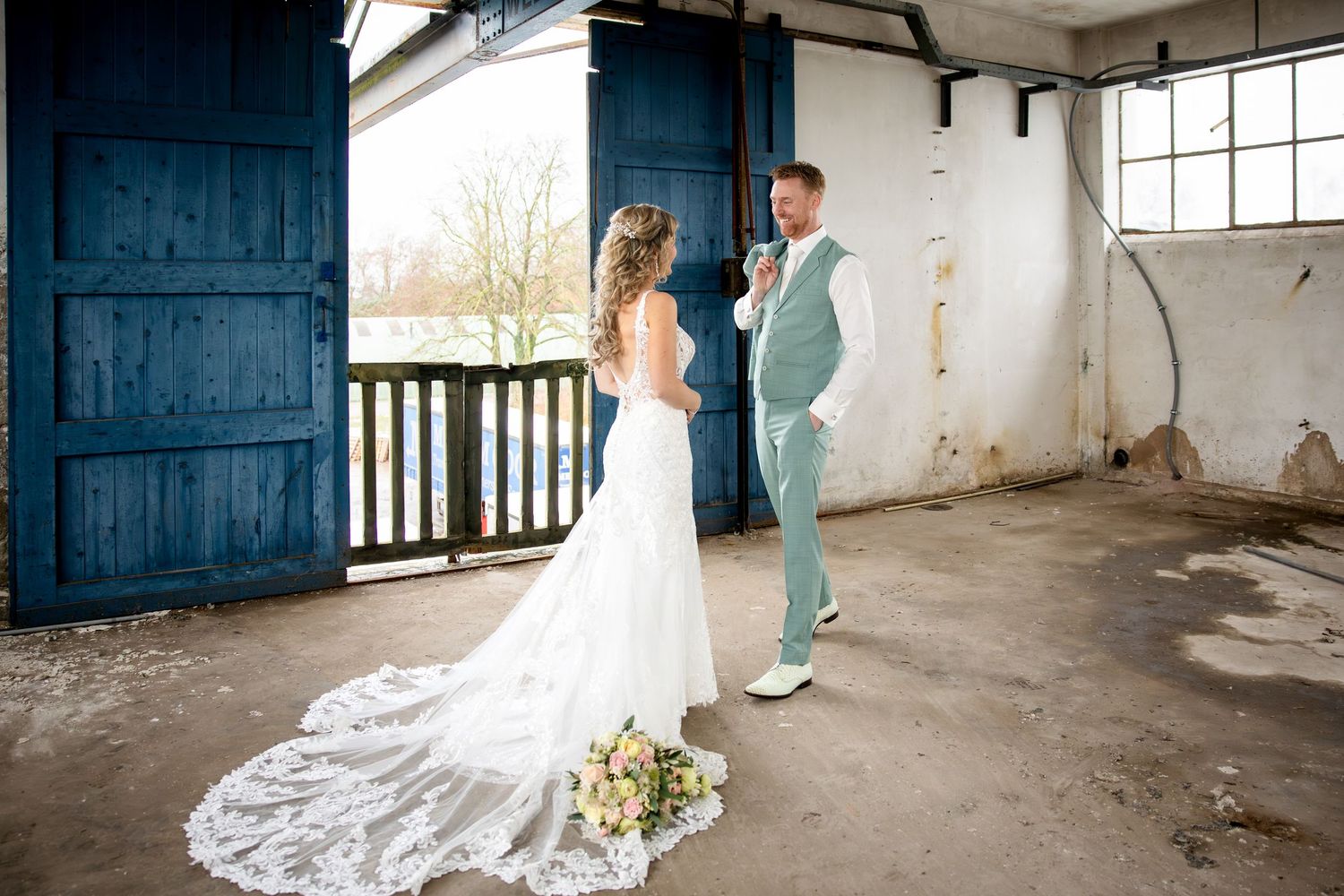 A couple in wedding attire poses in an industrial setting with rustic blue doors and white walls.