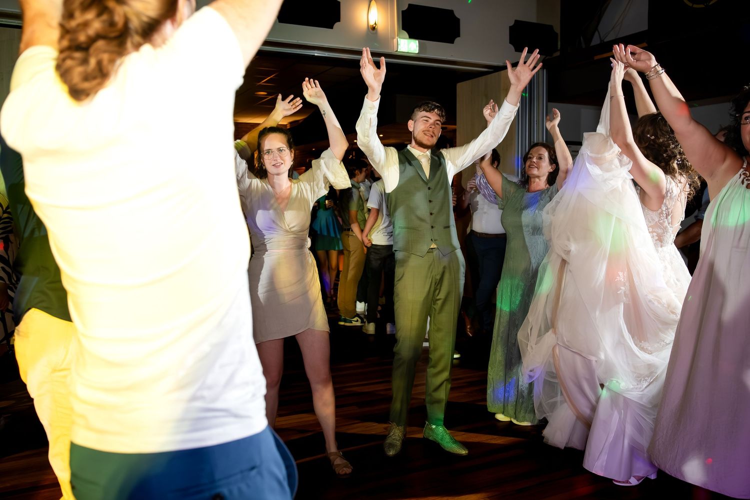 Wedding guests dancing and celebrating on a lively dance floor with colorful lighting.