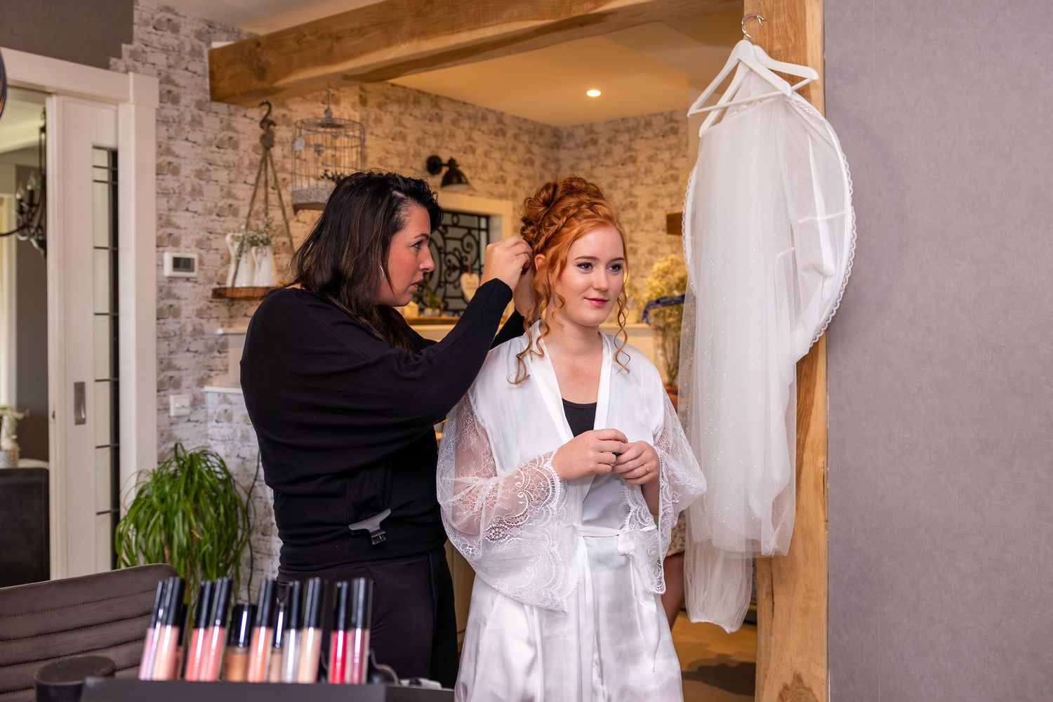 A bride getting ready in a white lace dress while others assist with wedding preparations.