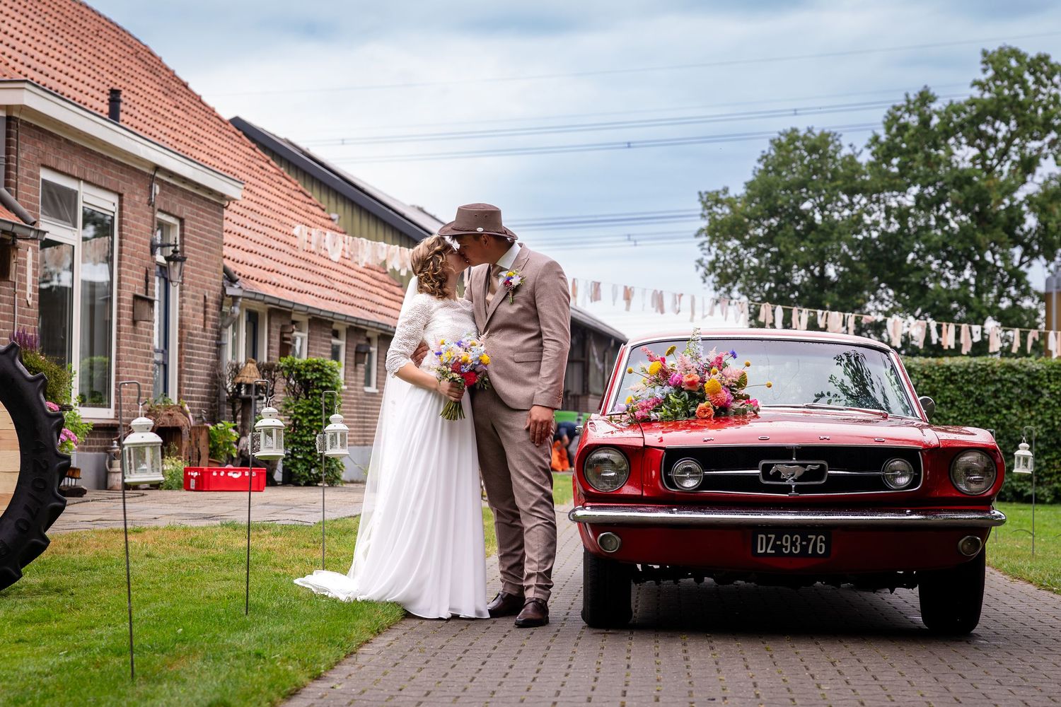 A classic red vintage car parked outside a brick building during a wedding celebration.