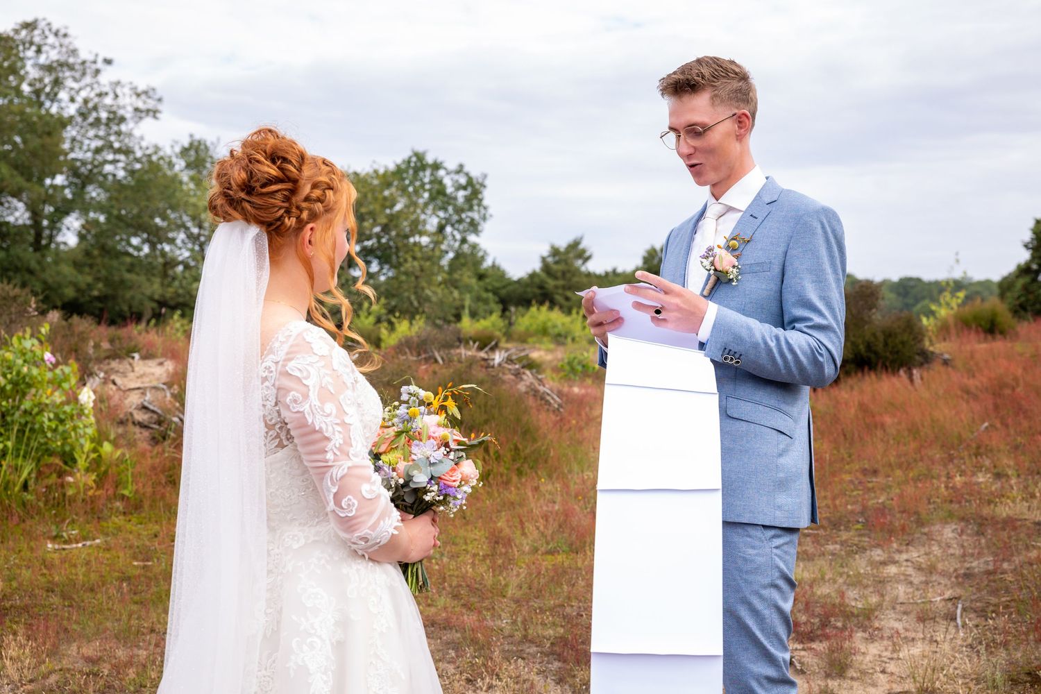 An outdoor wedding ceremony with the couple exchanging vows against a natural landscape.