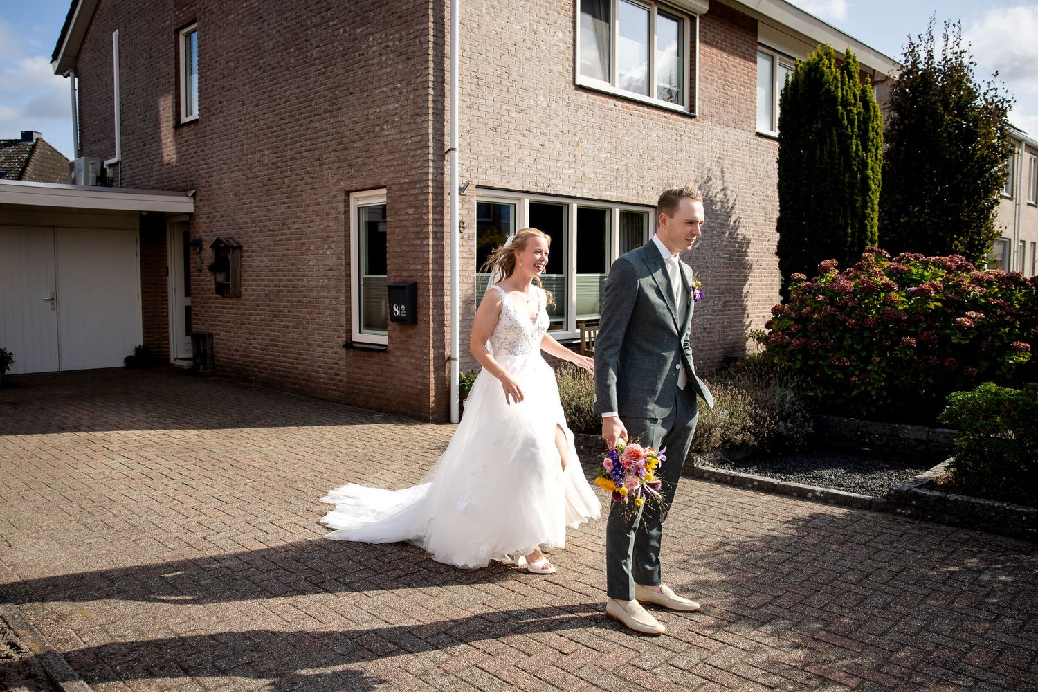 A wedding couple shares a romantic moment outside a brick building on a sunny day.
Een bruidspaar beleeft een romantisch moment buiten een