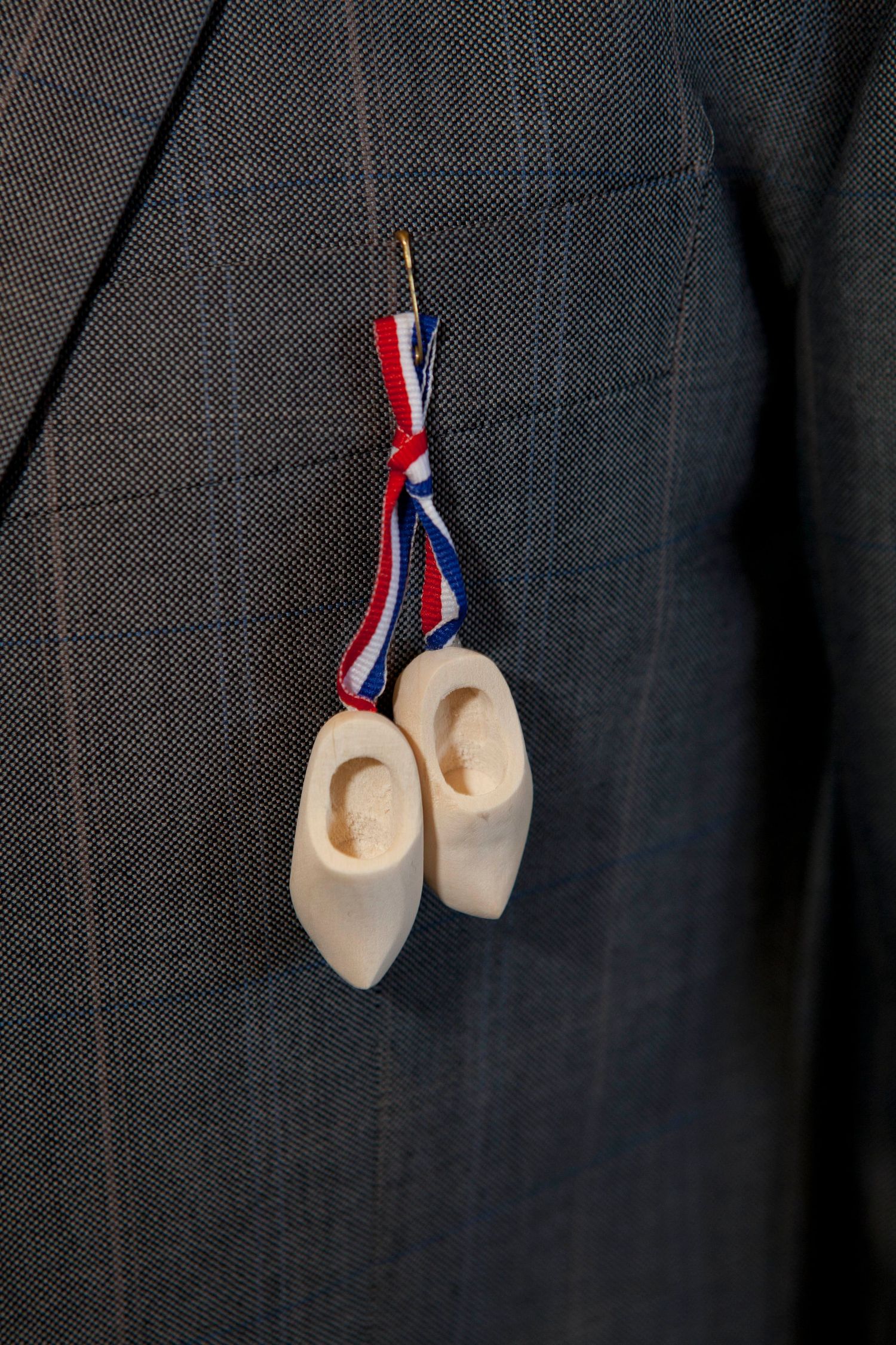 Small wooden Dutch clogs hanging on a dark fabric background with red white and blue ribbons attached.
