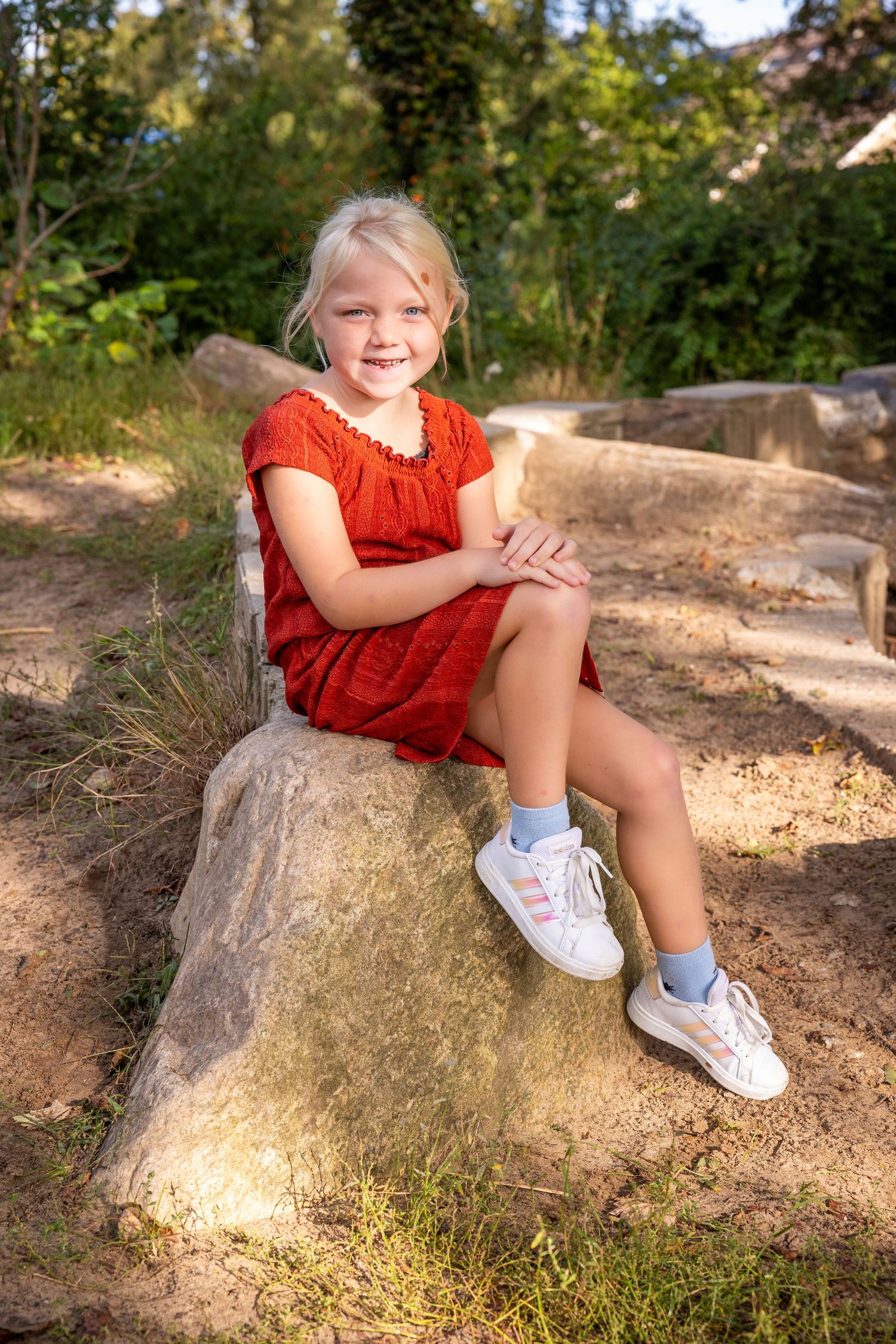 A series of outdoor photos showing someone in a bright red dress sitting on a large natural rock formation in sunlight.