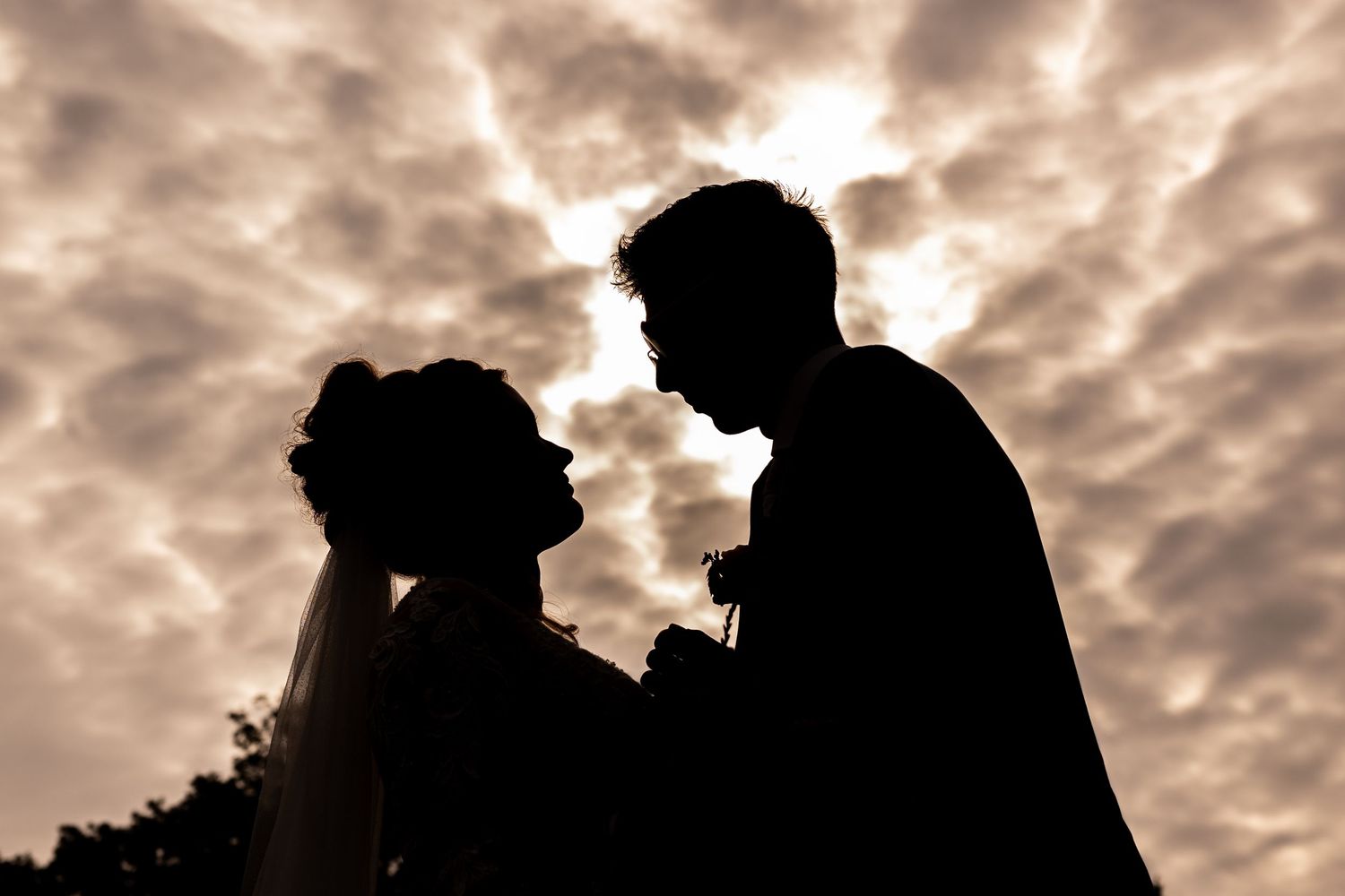 Silhouette of a wedding couple against dramatic cloudy sunset sky.