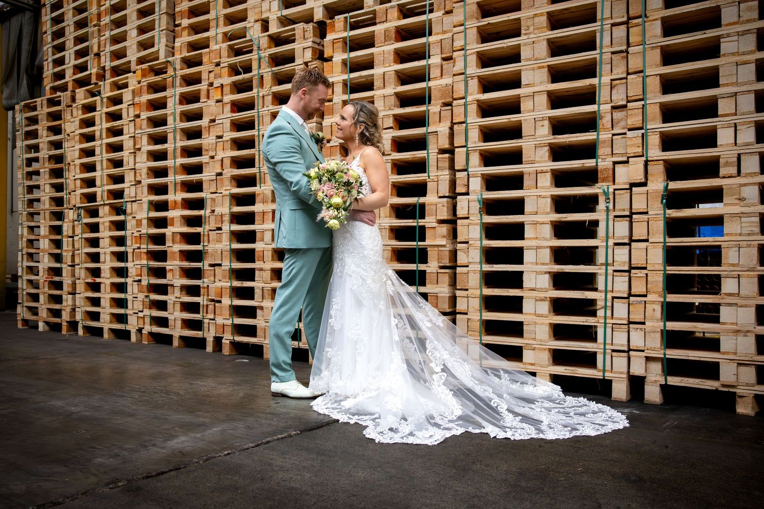 Romantic couple poses in front of rustic wooden pallet wall at a wedding venue.