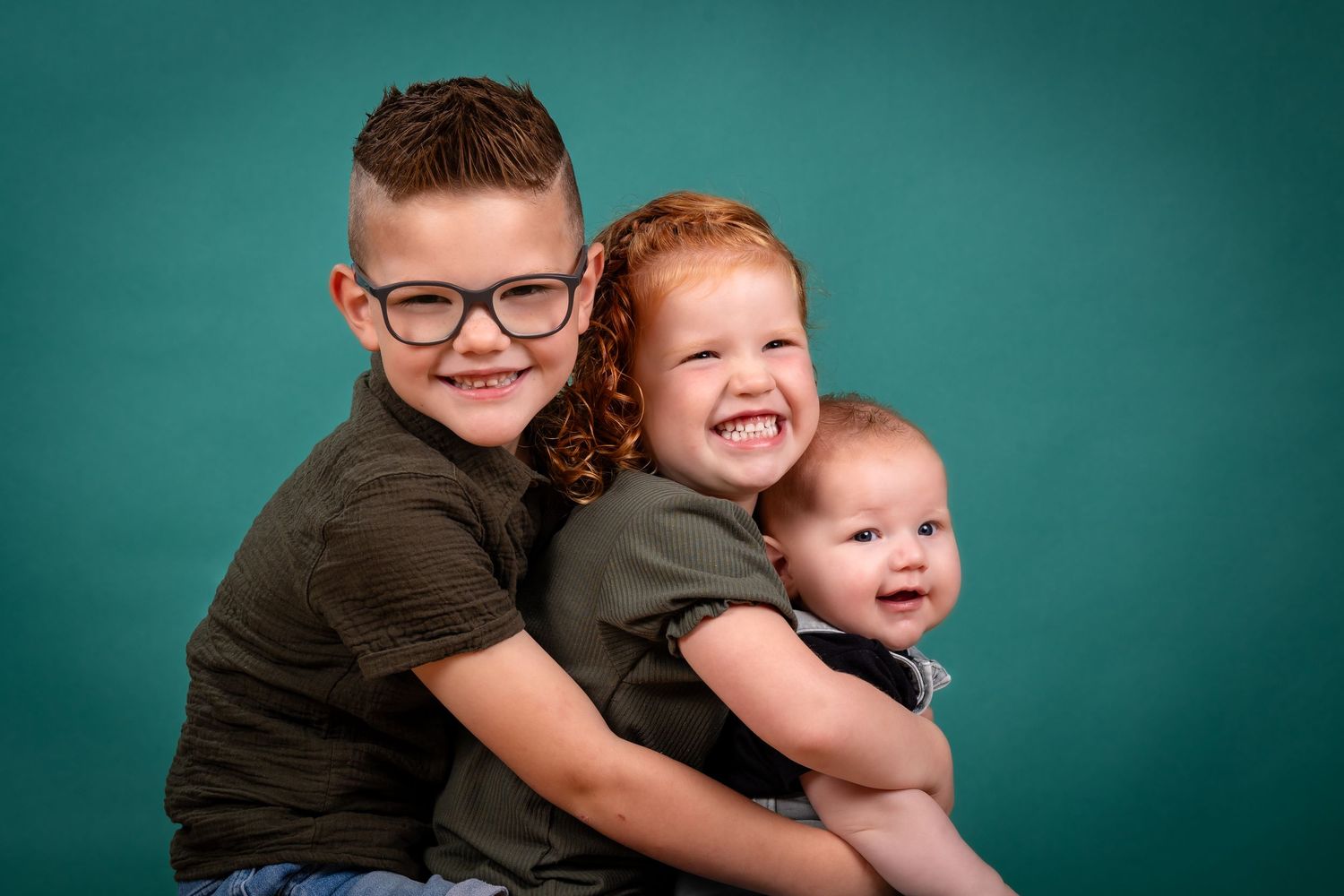 Two children in dark shirts pose playfully against a teal studio backdrop.
