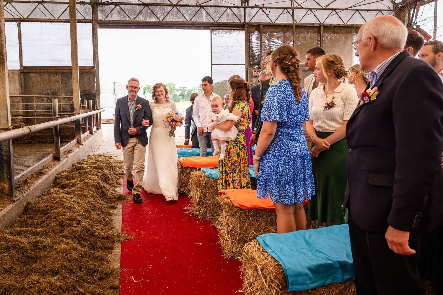Rustic barn wedding venue interior with hay bales and red carpet for guest seating.