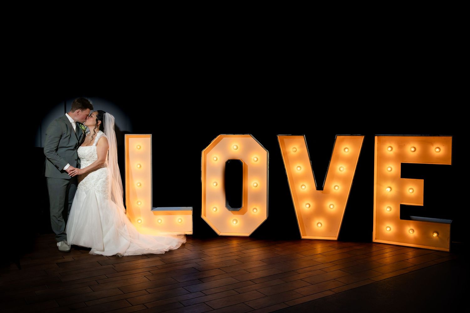 bruidspaar houdt elkaar liefdevol vast naast verlichte letters LOVE