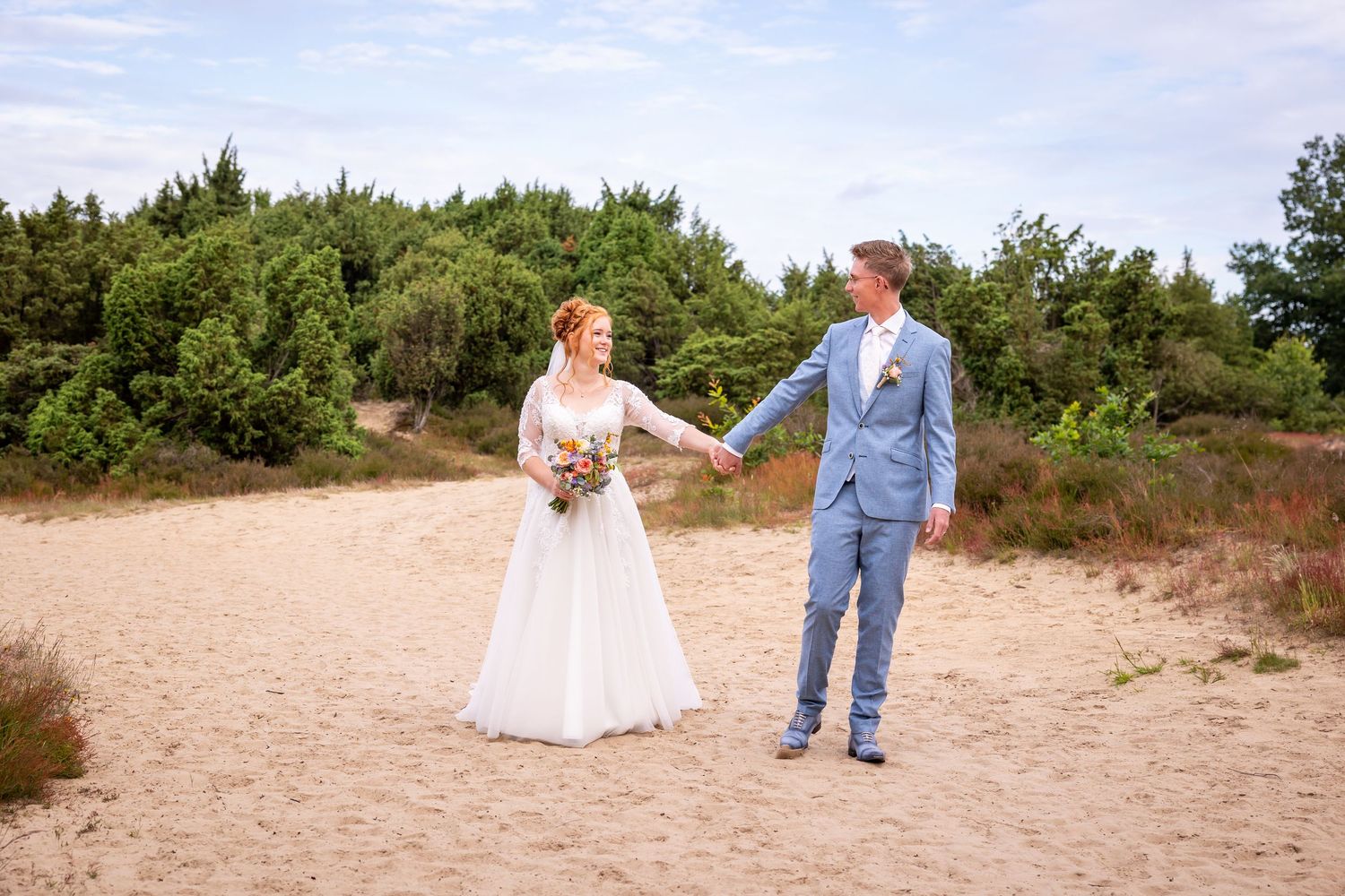 A couple holding hands in a natural sandy landscape during their wedding.