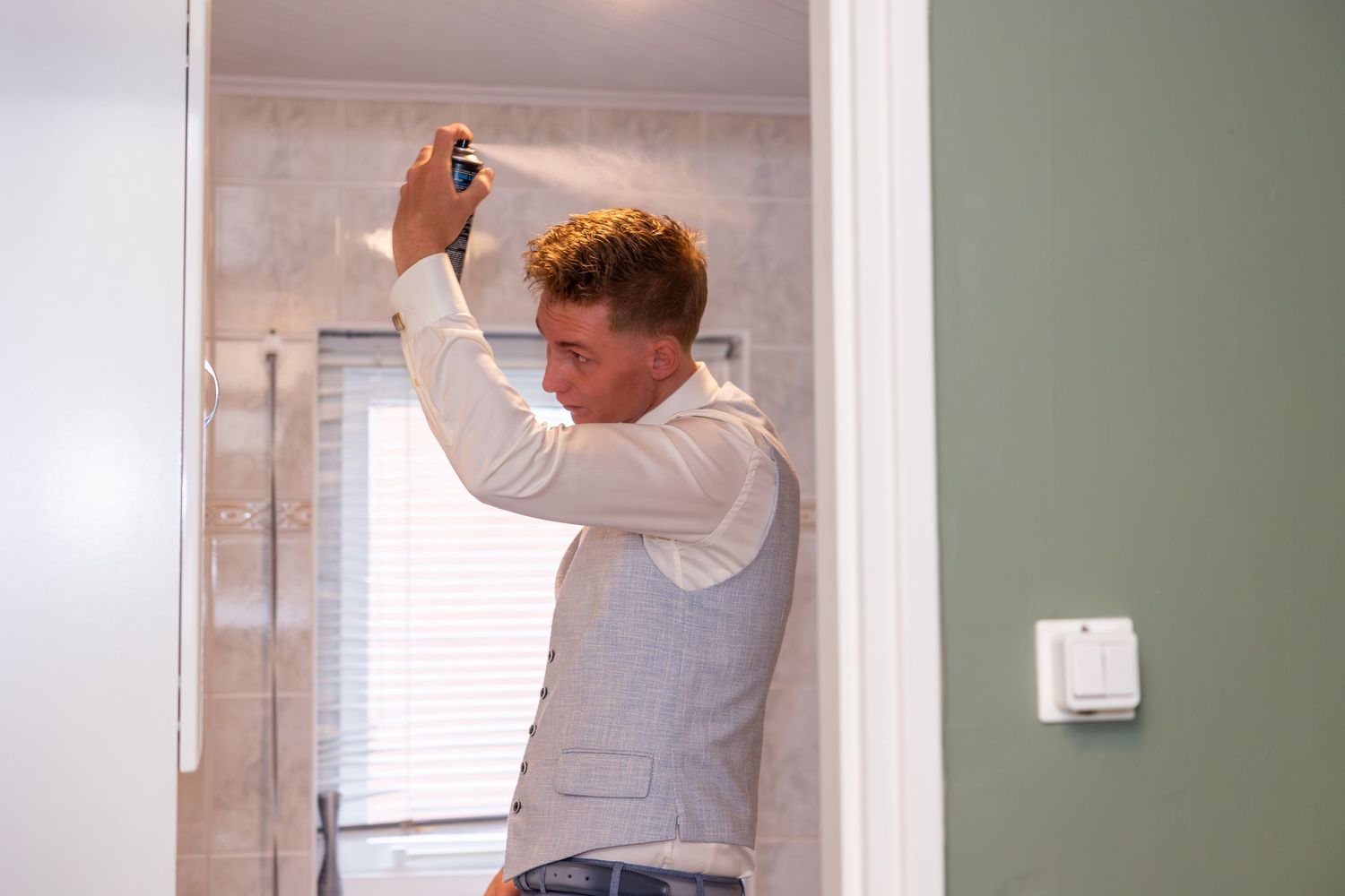 Person applying hair product while getting ready in bathroom.