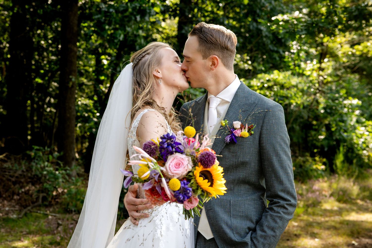 bruidspaar zoent elkaar en houdt bloemen vast in een mooi bos