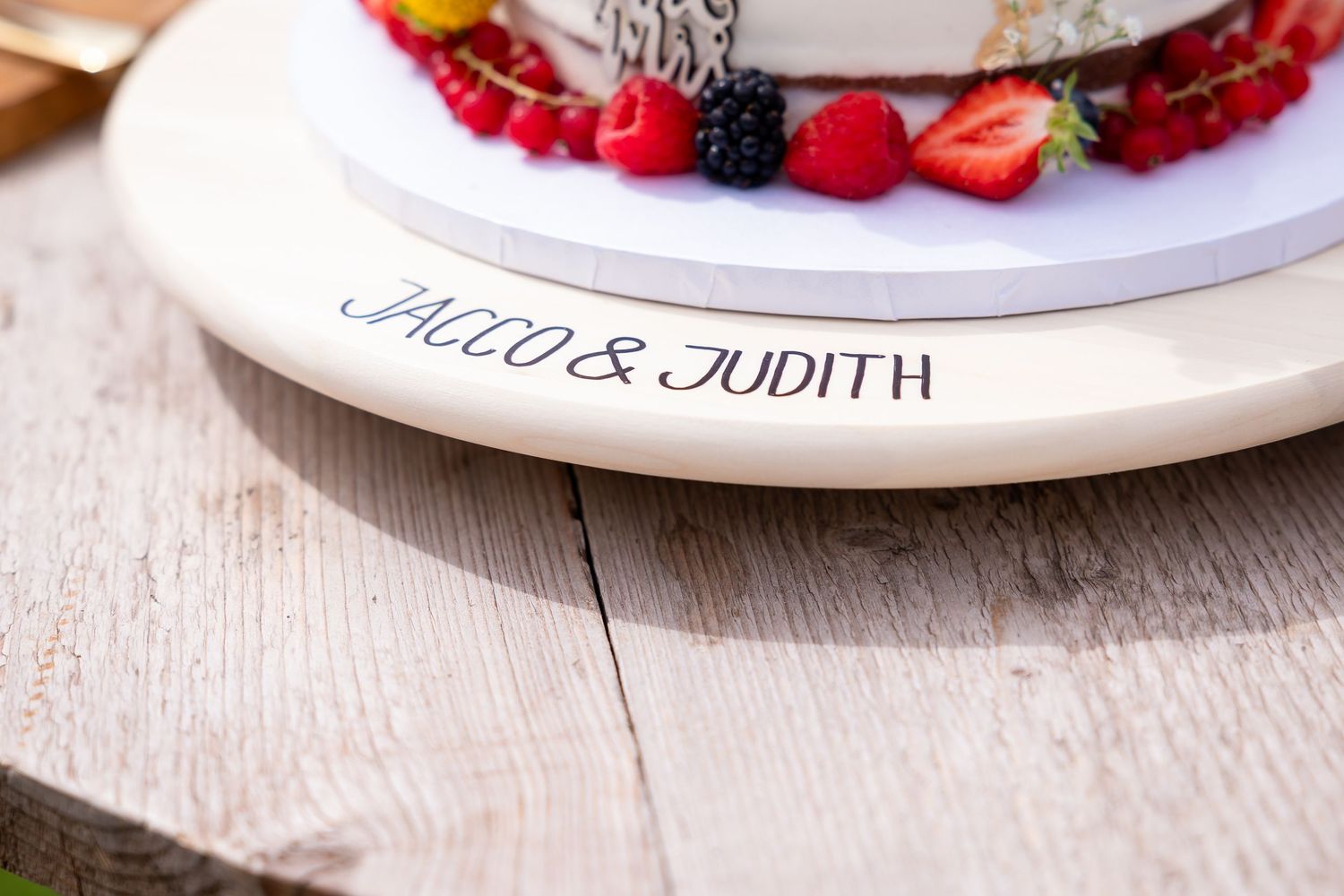 White wedding cake plate decorated with fresh red berries and fruit on a wooden surface.