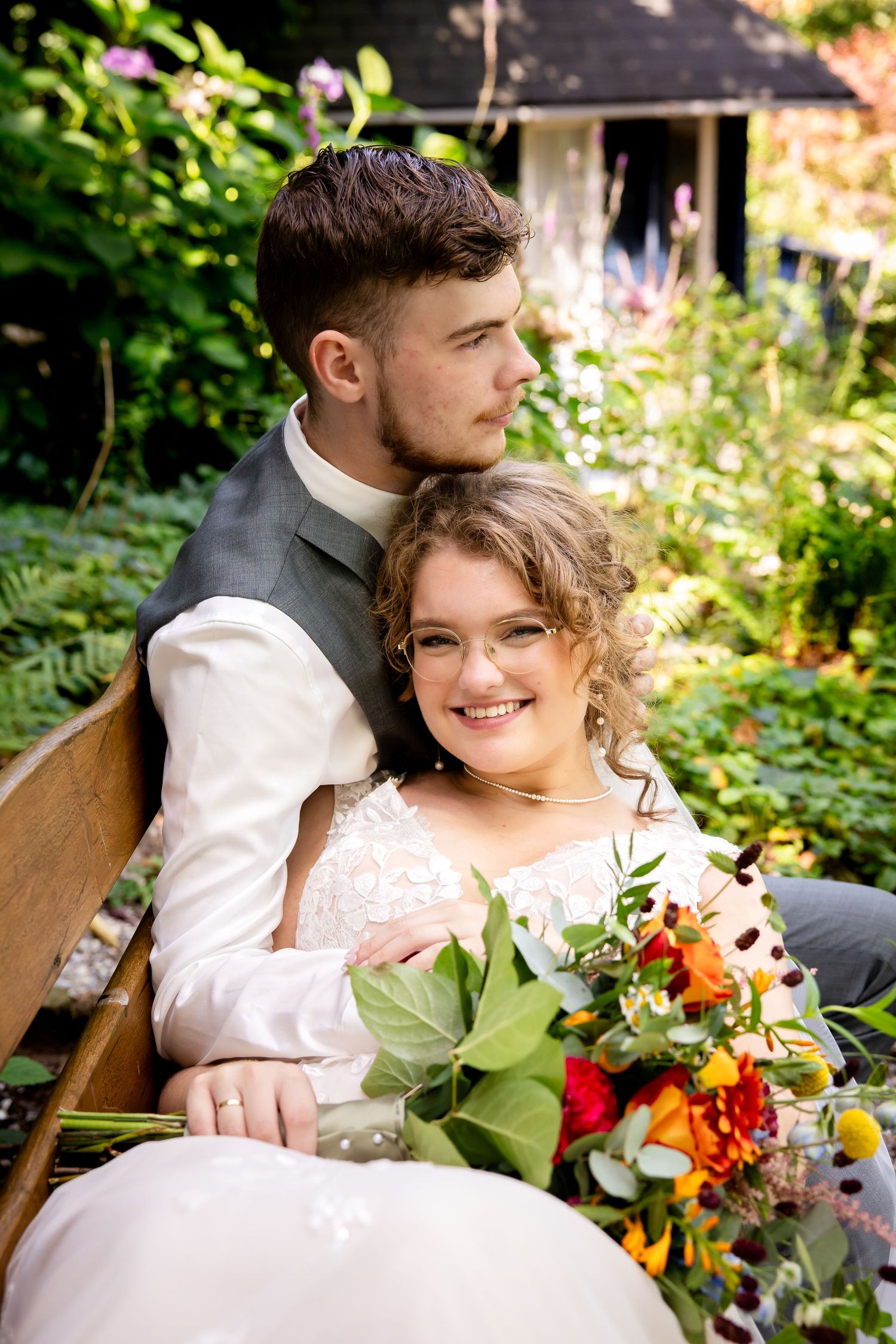 Couple seated on wooden bench with colorful wildflower bouquet in garden setting.