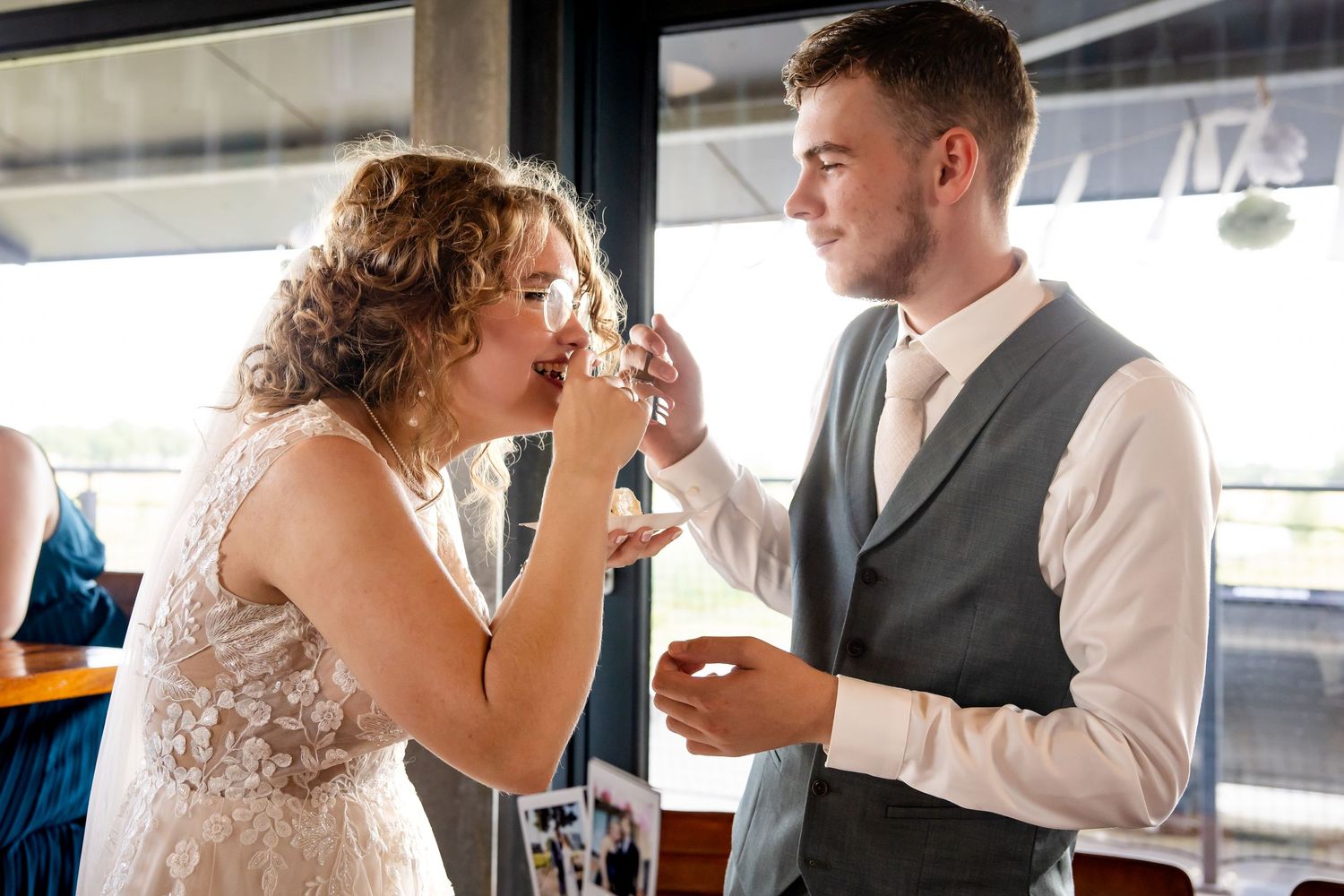 Couple shares cake and laughter during their wedding reception at an indoor venue.