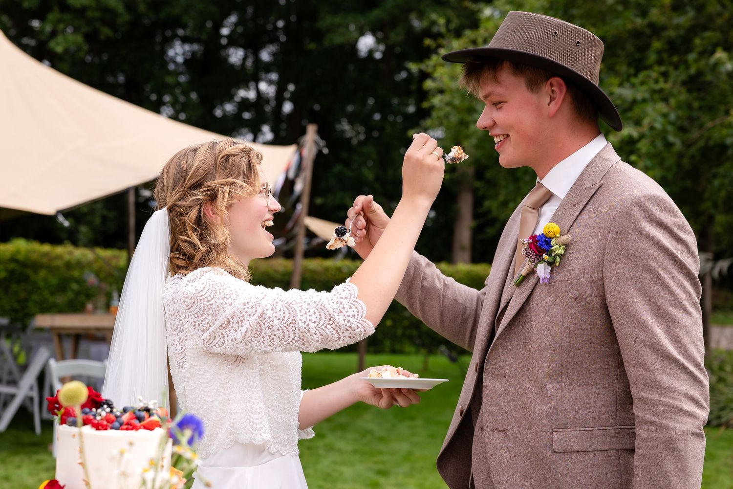 Playful cake cutting moment at an outdoor wedding reception.