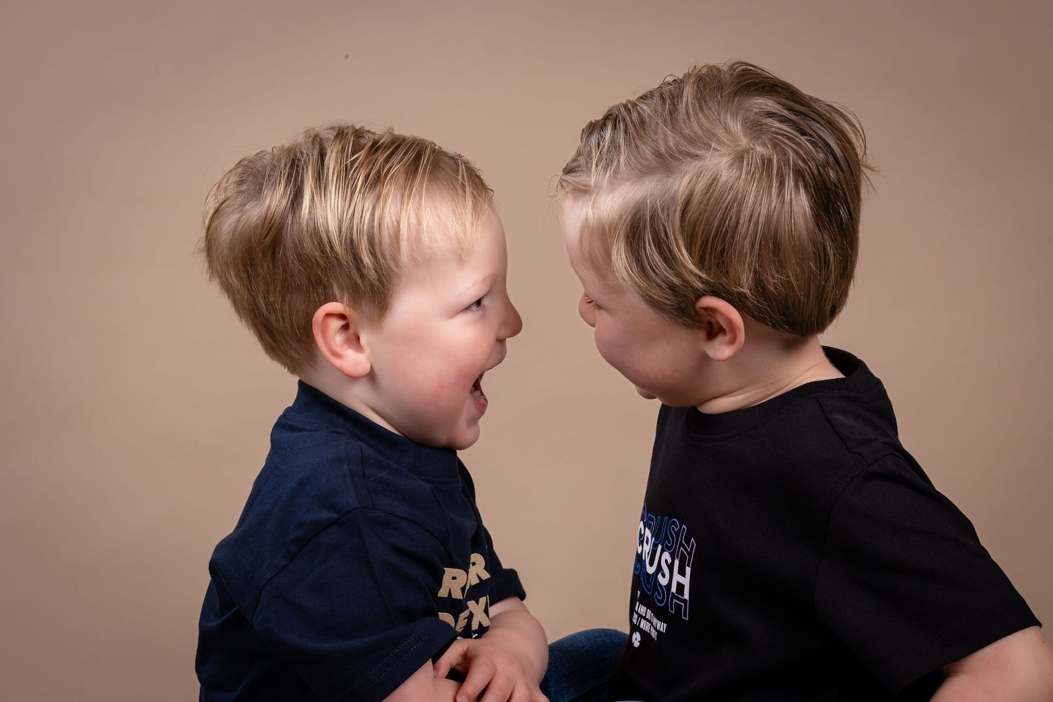 Two toddlers in navy blue sweaters interact with each other in a series of candid moments.