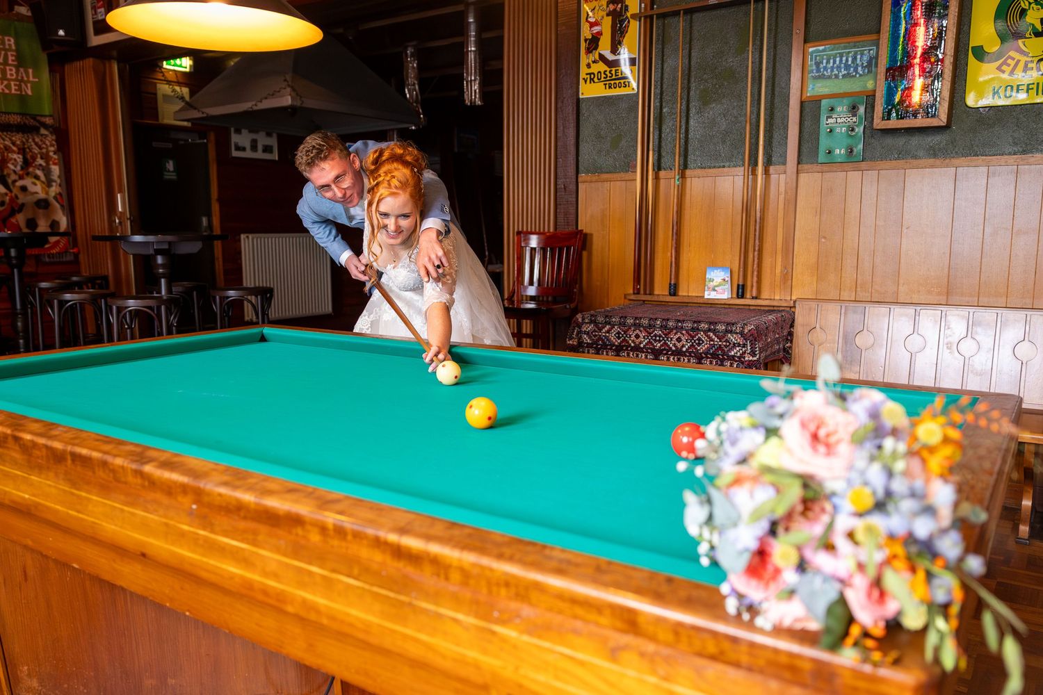 A couple takes aim at a pool shot together on a green felt table.