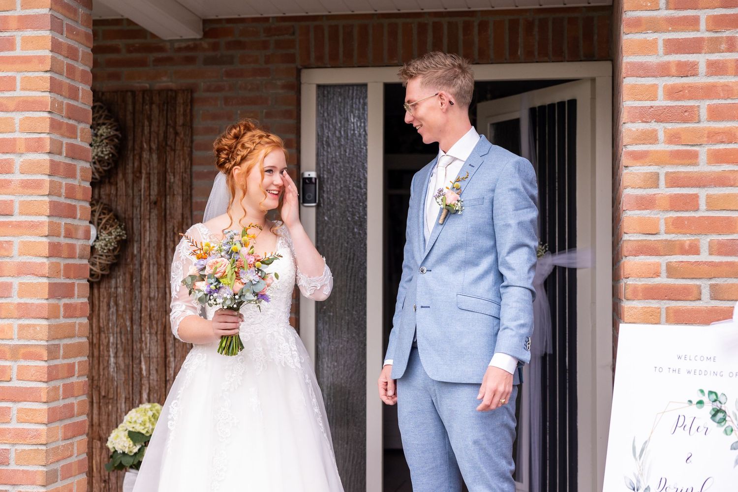 A joyful wedding moment captured on a brick porch as the couple shares their first look.