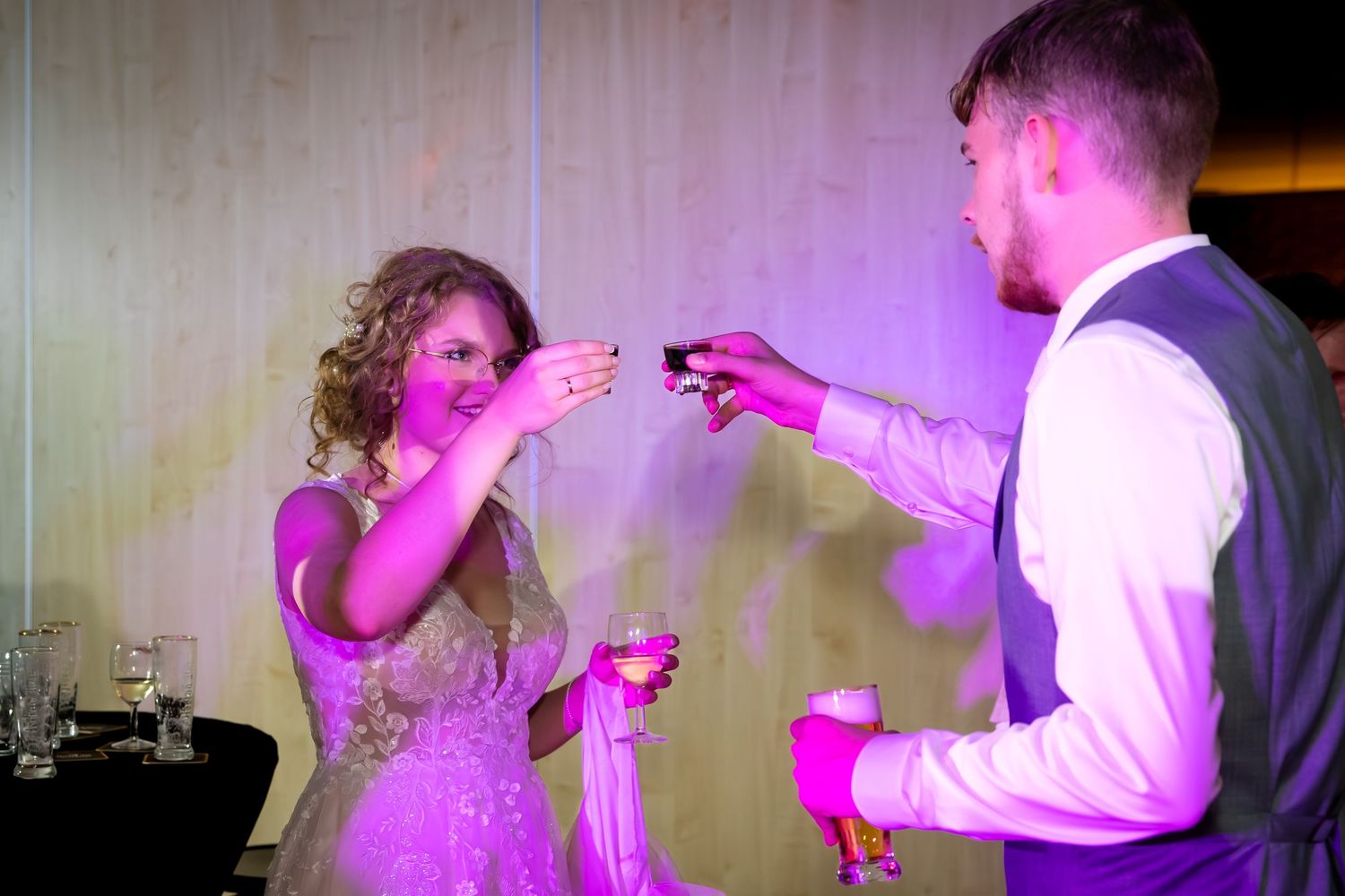 Wedding party dancing under purple lighting at an indoor reception venue.