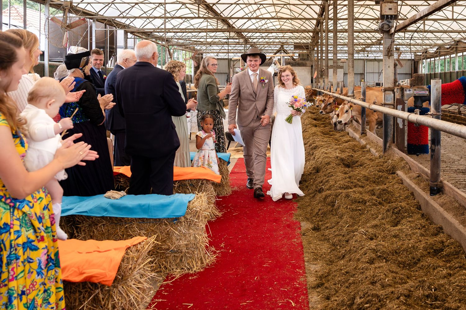 Wedding celebration in a barn with hay bales and red carpet decor.