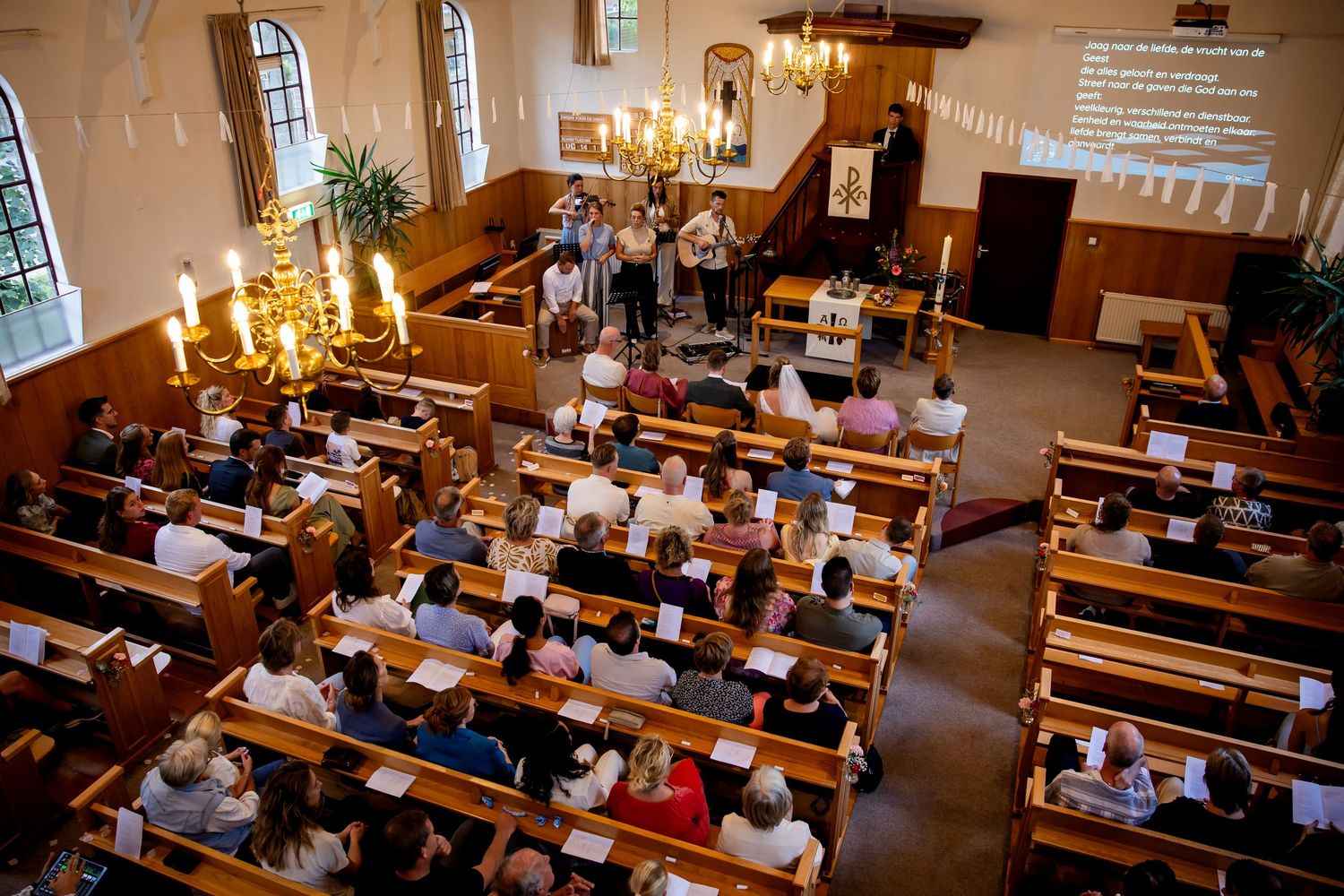 Kerk vol gasten tijdens huwelijksceremonie met kroonluchterverlichting.