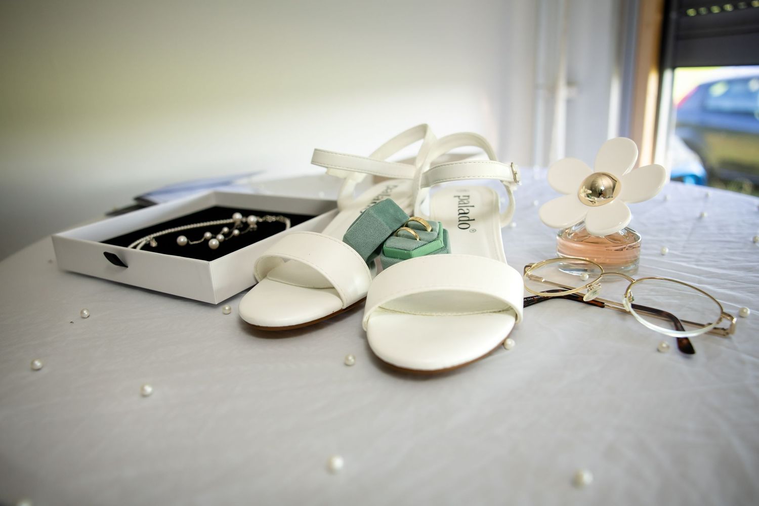 Wedding accessories including white shoes and jewelry laid out on surface.