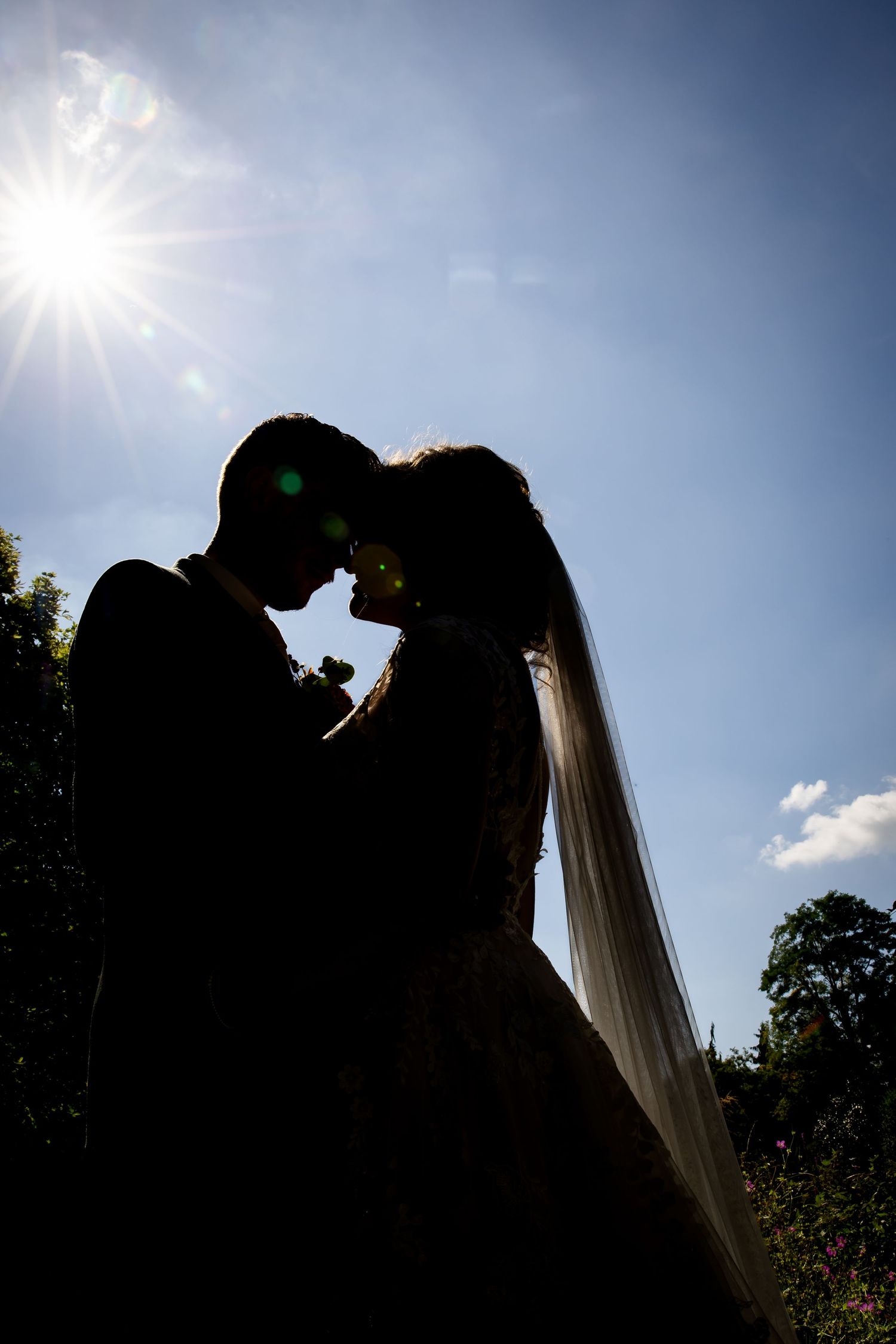 Silhouetted couple against bright blue sky creating romantic wedding portrait.