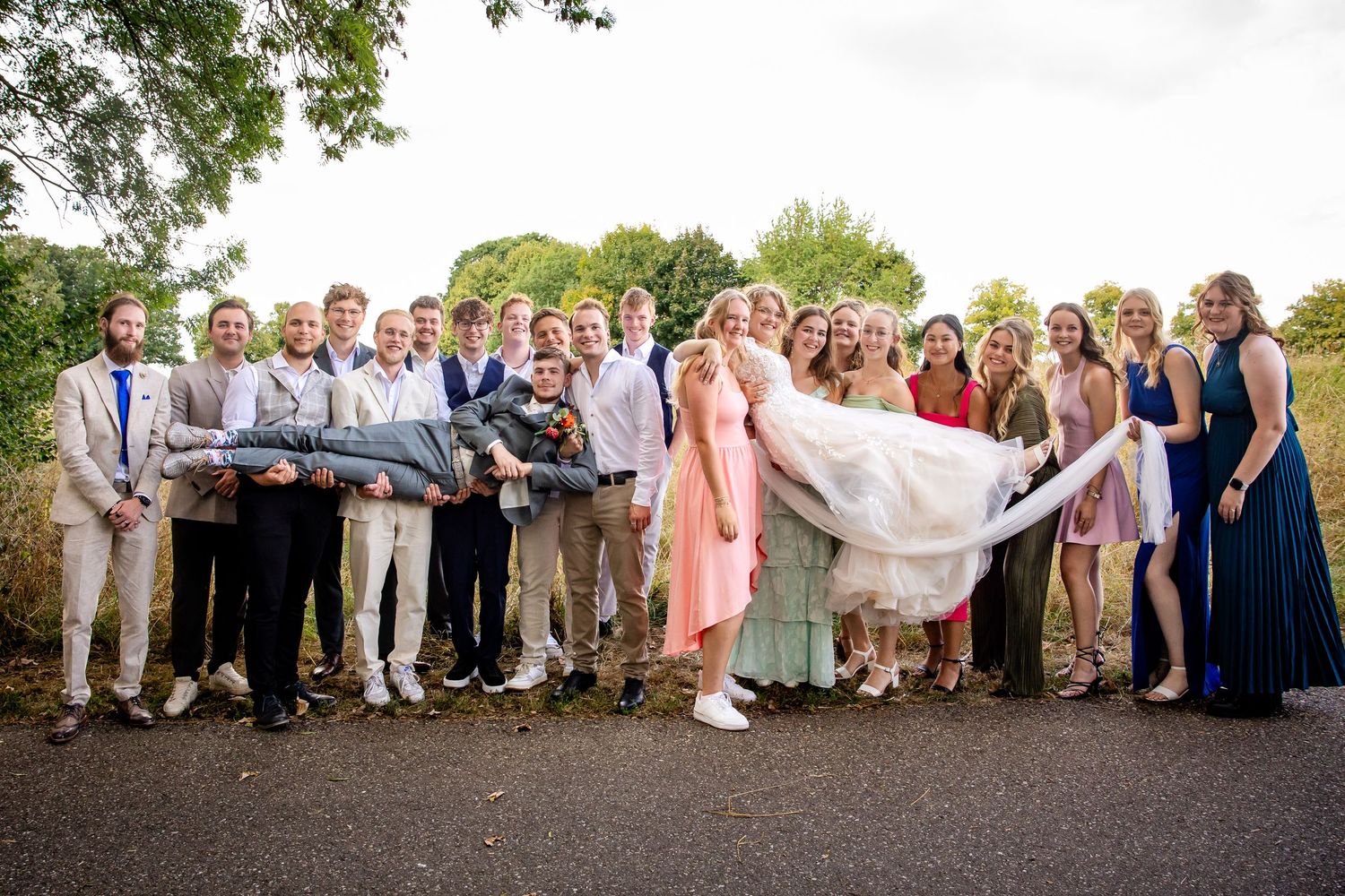Large wedding group photo with guests arranged in formal lineup outdoors.