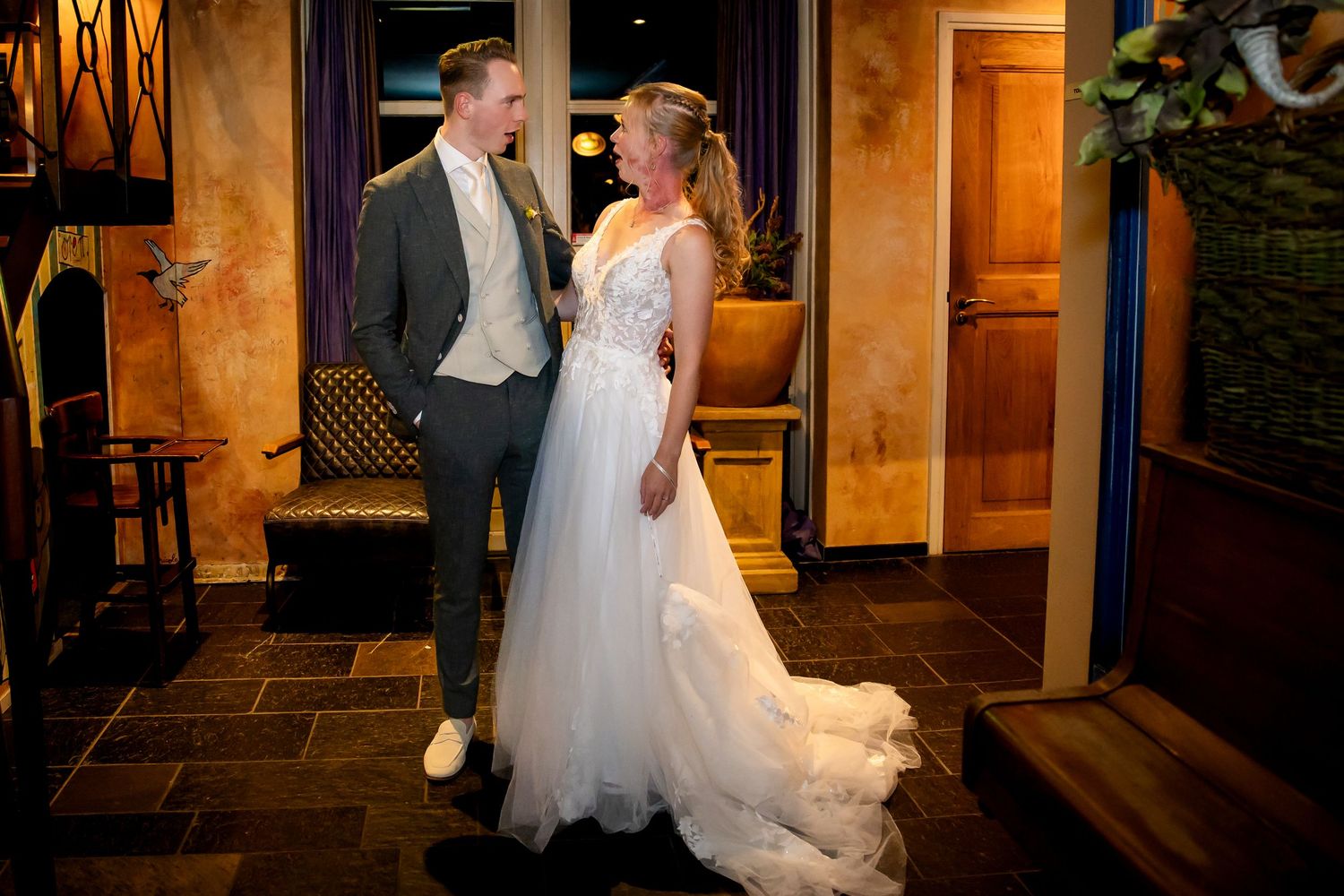 Een bruidspaar poseert samen in een elegant verlichte hal.