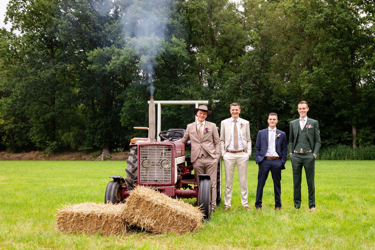 Wedding party posing in front of rustic farm equipment and hay bales.