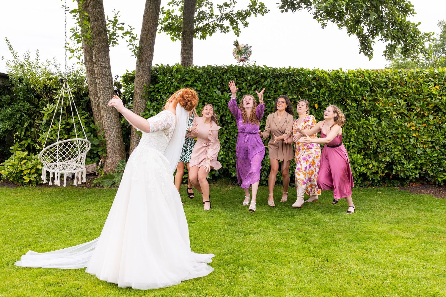 Wedding party poses playfully on lawn with bridesmaids in pink and purple dresses.