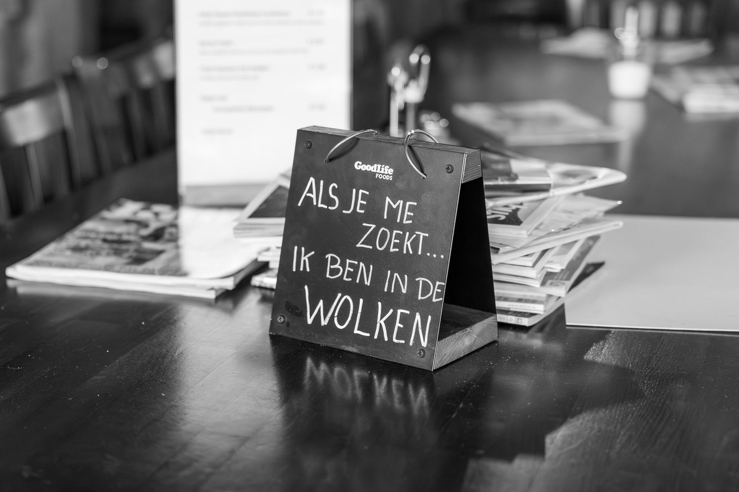 A black and white photo of a sign in Dutch text on a dark table.
