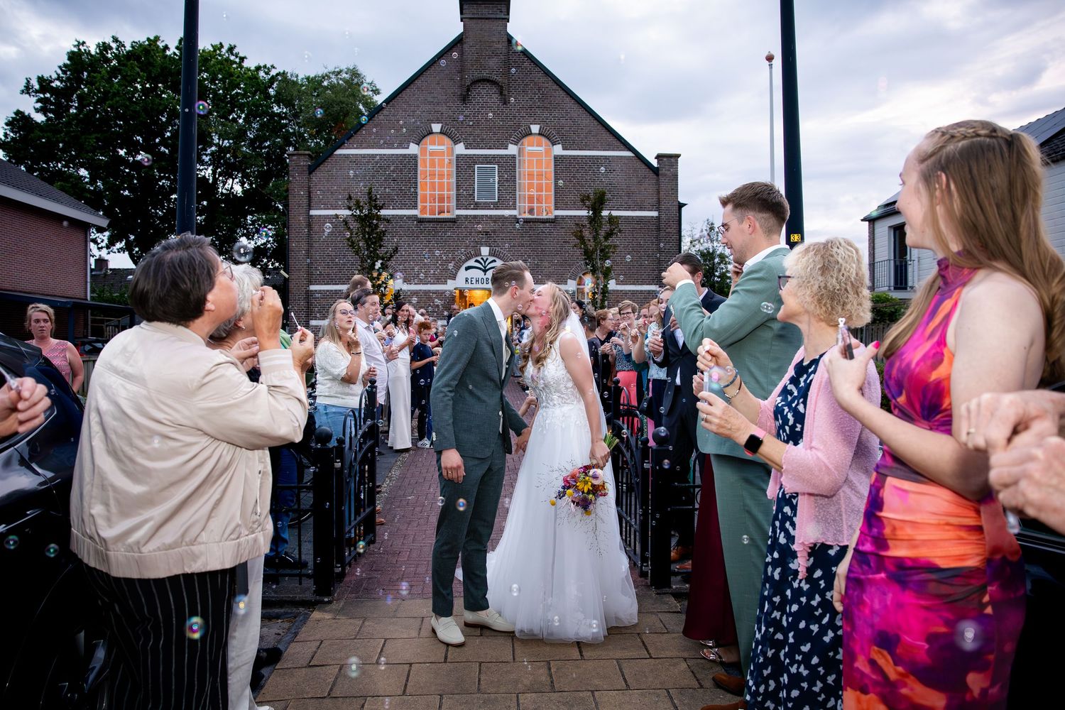 Bruiloftsgasten verzamelen zich buiten een stenen kerkgebouw om het pasgetrouwde stel te vieren.
